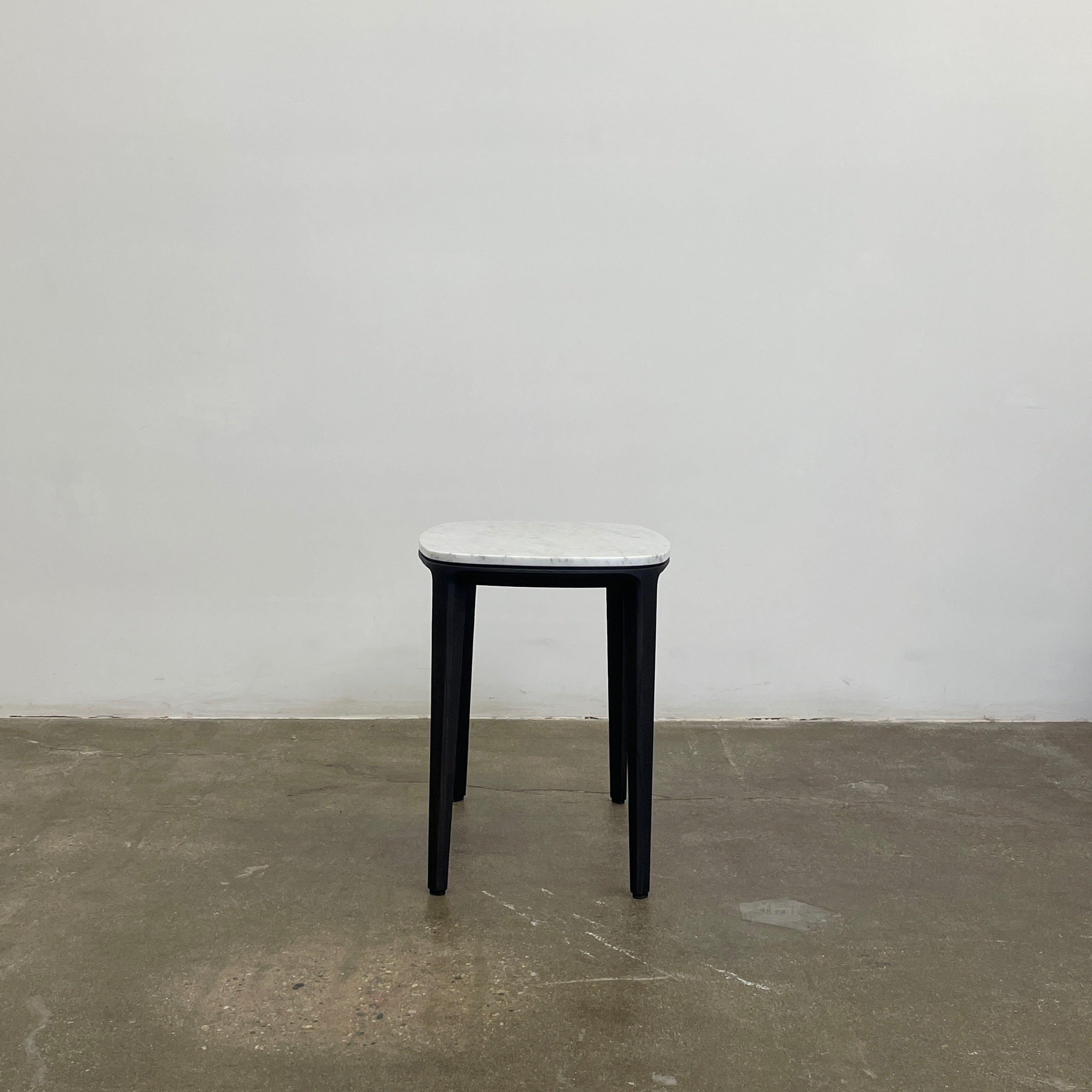 The Poliform Henry Marble Side Table, by Poliform, showcases an elegant small oval design with a luxurious Carrara marble top. It stands gracefully on four black Elm legs against a minimalist white backdrop.