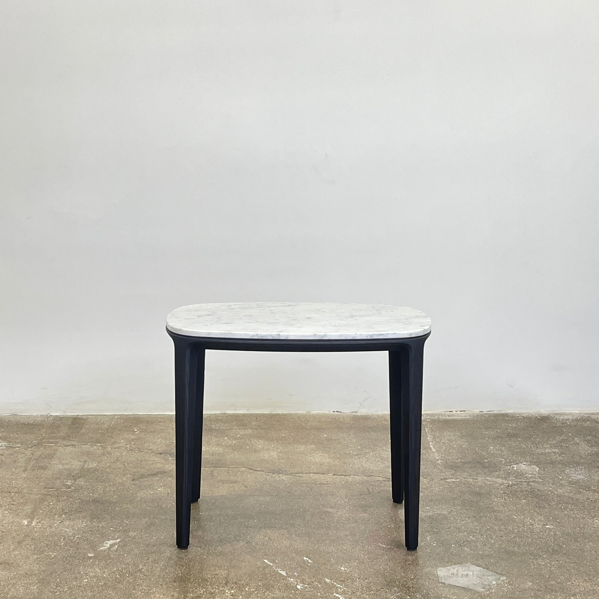 The Poliform Henry Marble Side Table, by Poliform, showcases an elegant small oval design with a luxurious Carrara marble top. It stands gracefully on four black Elm legs against a minimalist white backdrop.