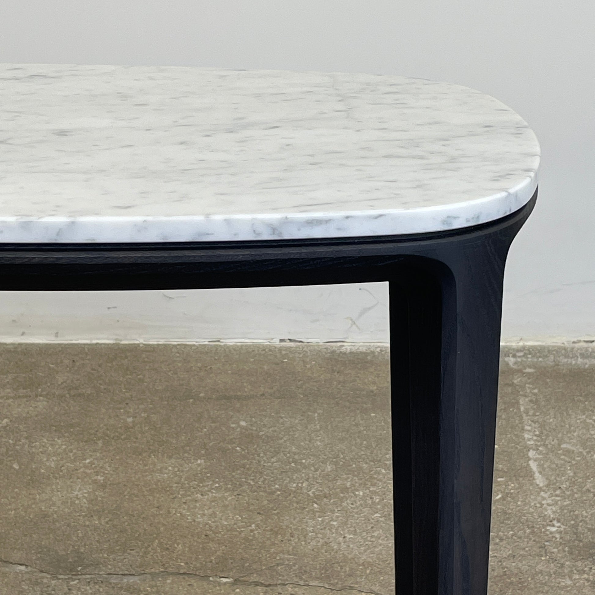 The Poliform Henry Marble Side Table, by Poliform, showcases an elegant small oval design with a luxurious Carrara marble top. It stands gracefully on four black Elm legs against a minimalist white backdrop.