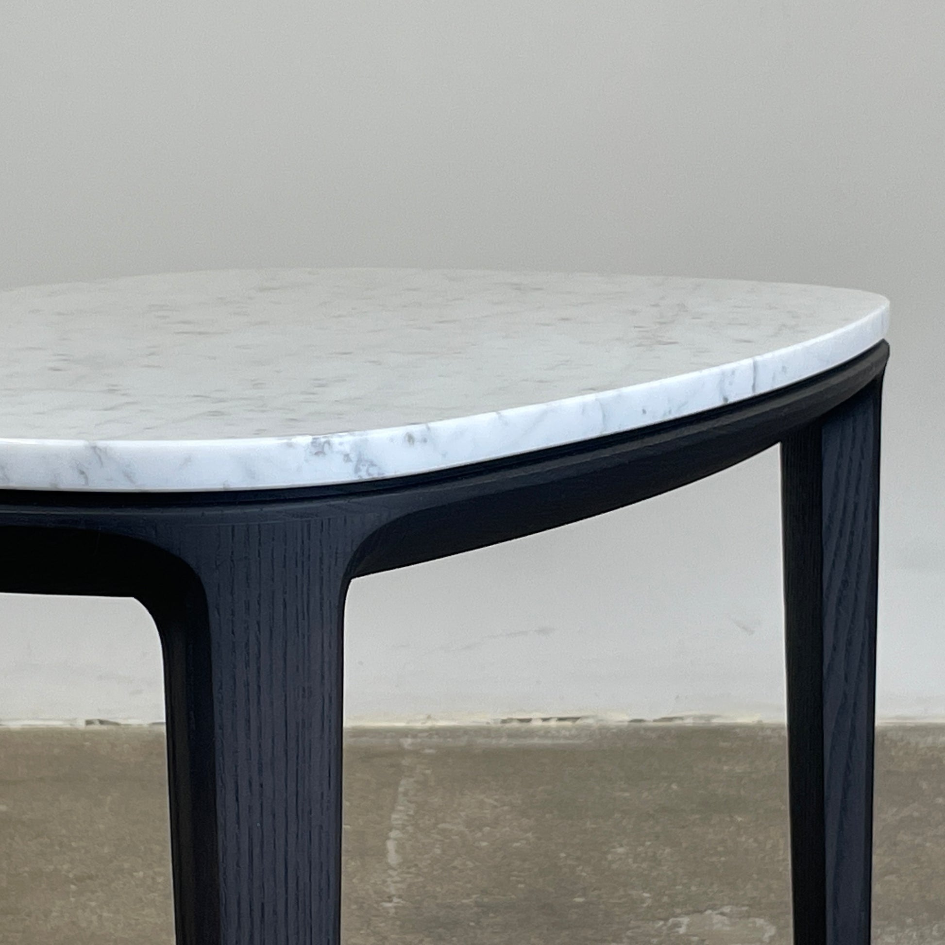 The Poliform Henry Marble Side Table, by Poliform, showcases an elegant small oval design with a luxurious Carrara marble top. It stands gracefully on four black Elm legs against a minimalist white backdrop.
