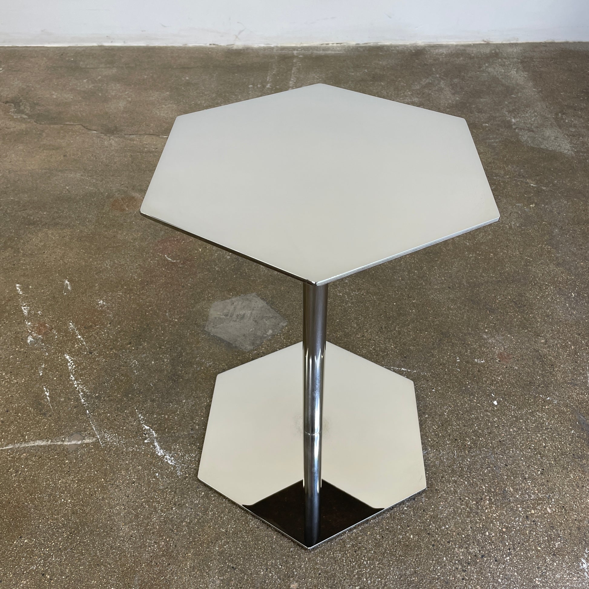 The Minotti Brisley Side Table by Rodolfo Dordoni features a stylish hexagonal metal surface supported by a central stand that flows into a matching base.