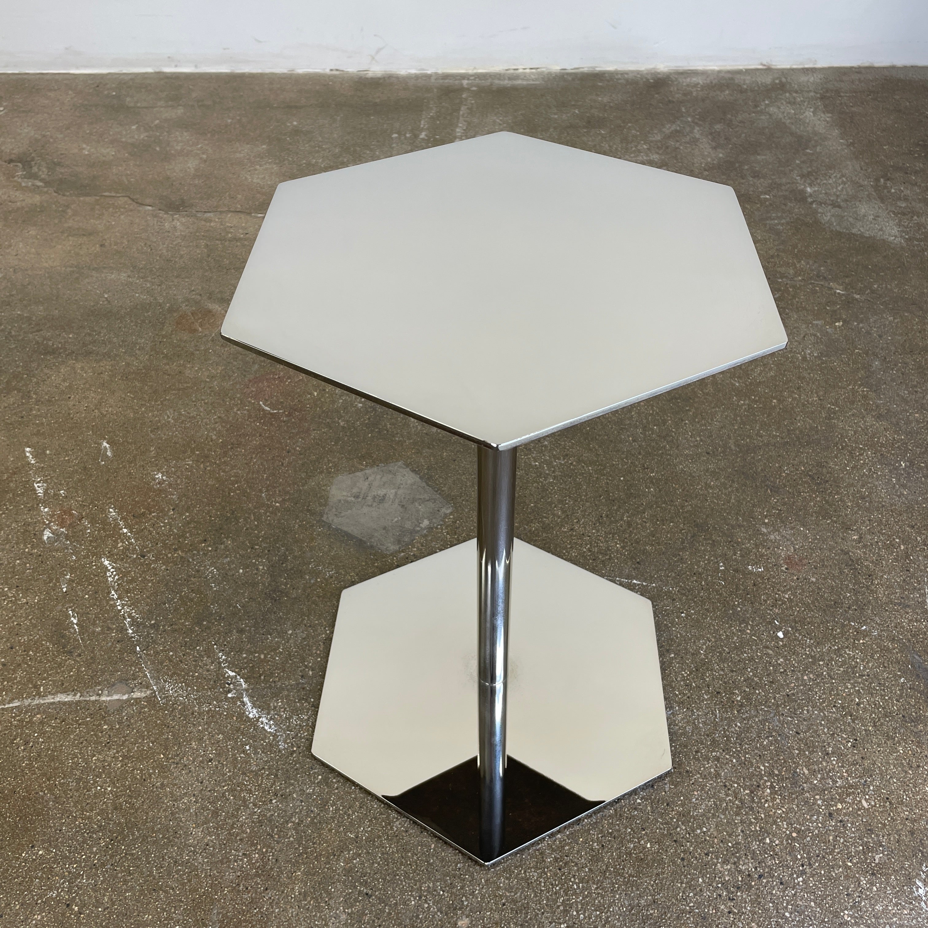 The Minotti Brisley Side Table by Rodolfo Dordoni features a stylish hexagonal metal surface supported by a central stand that flows into a matching base.