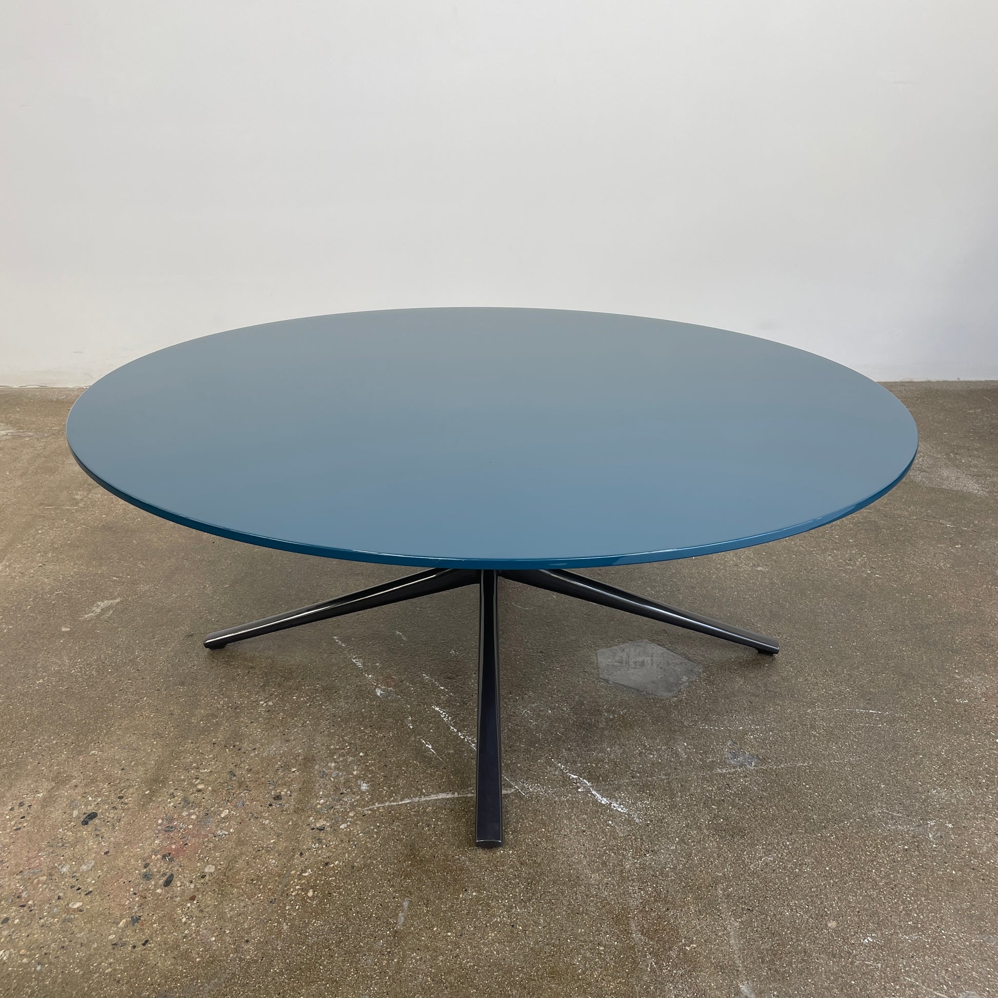The Poliform Mondrian Lacquered Coffee Table showcases a round blue top with a black, four-legged metal base against a white background.