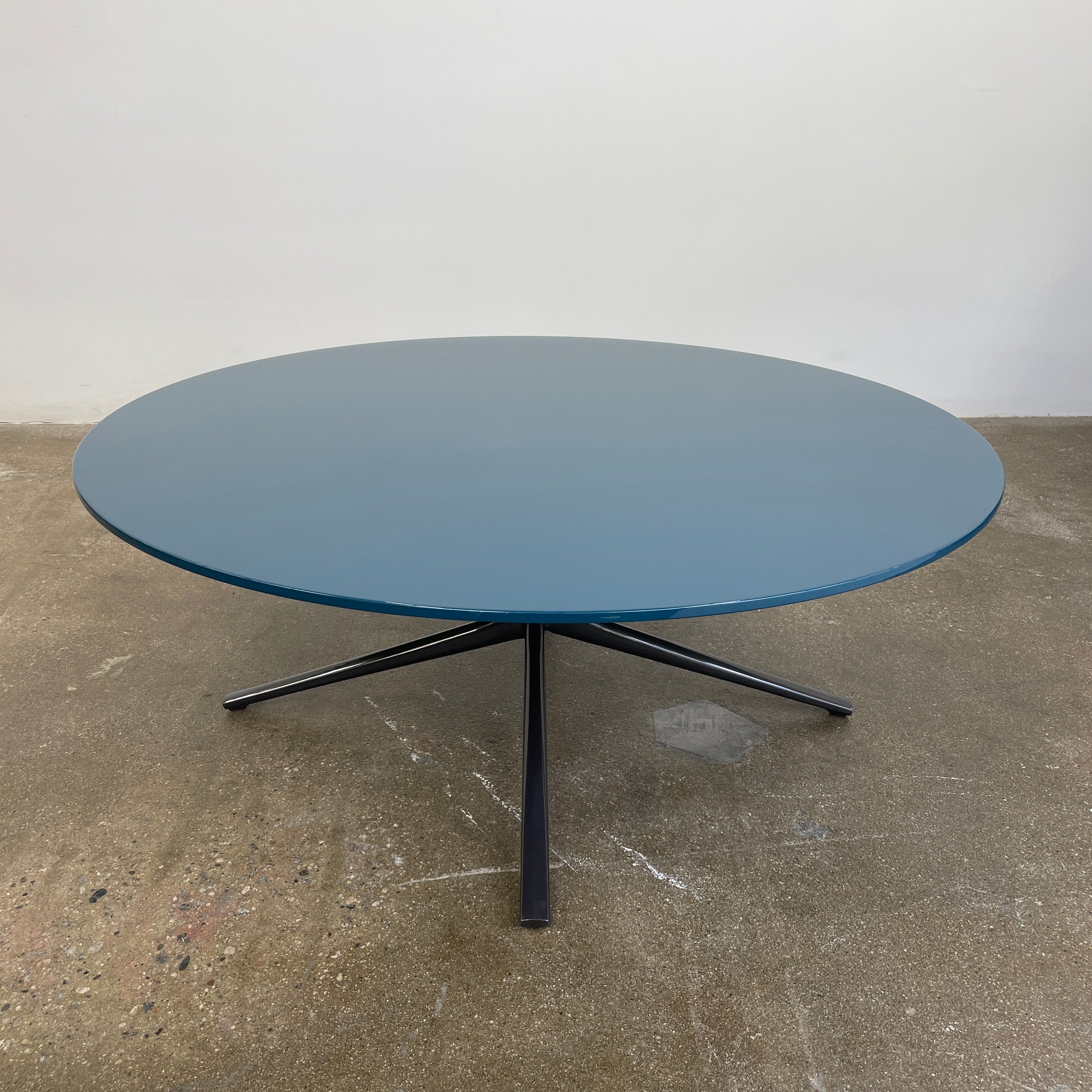 The Poliform Mondrian Lacquered Coffee Table showcases a round blue top with a black, four-legged metal base against a white background.