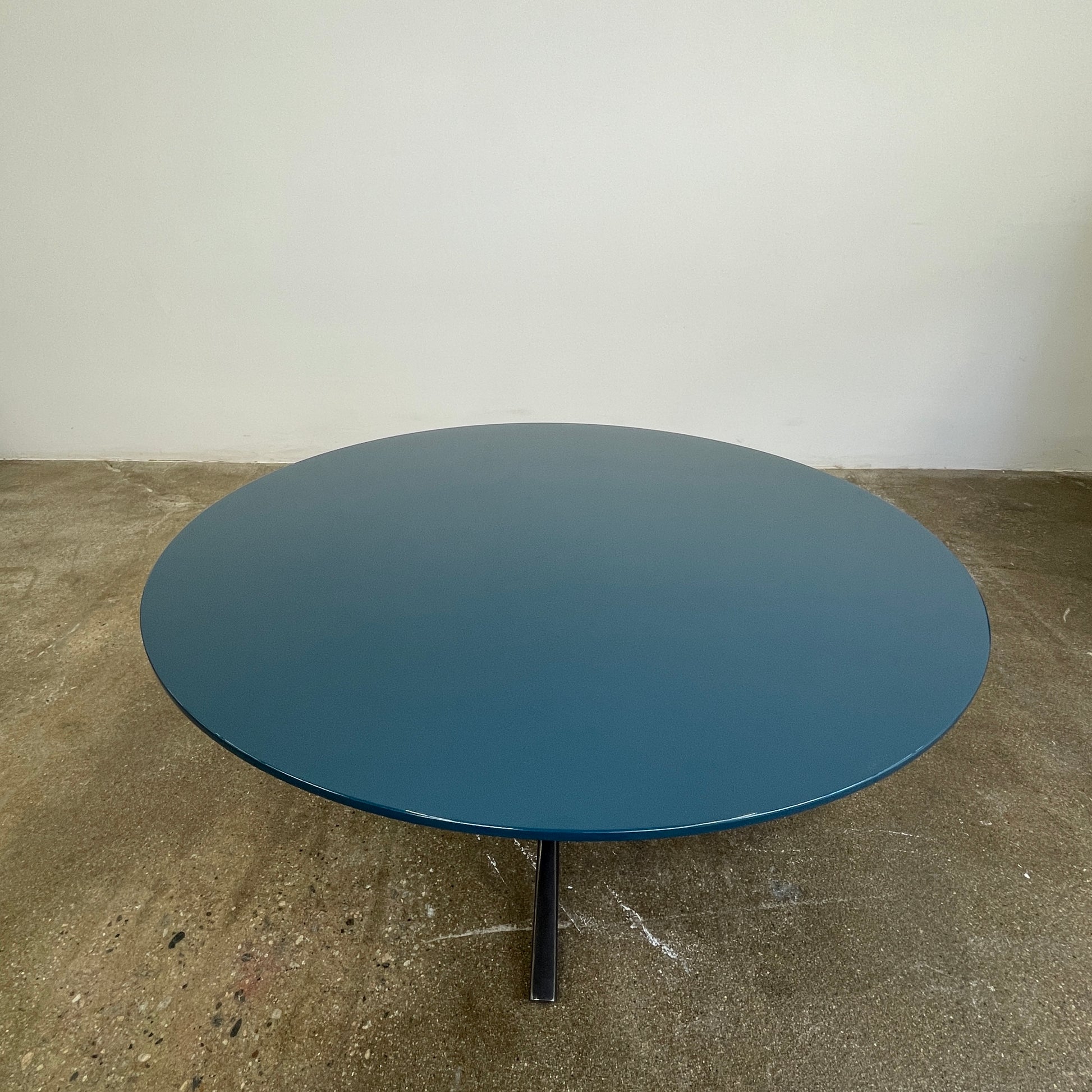 The Poliform Mondrian Lacquered Coffee Table showcases a round blue top with a black, four-legged metal base against a white background.