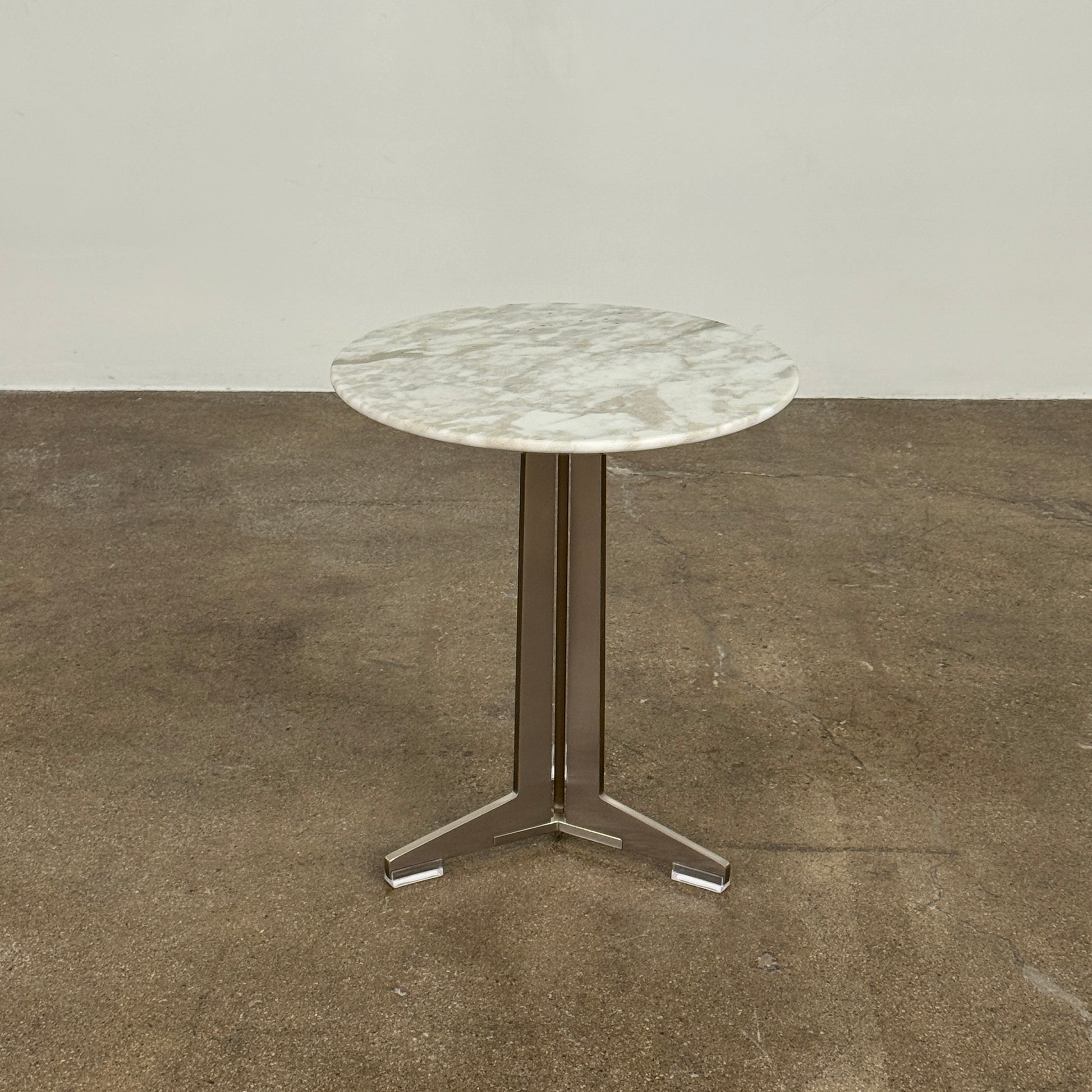 The Flexform Fly Small Table by Modern Resale is a chic side table with a white marble top and metal base, elegantly positioned on a polished concrete floor against a light-colored wall.