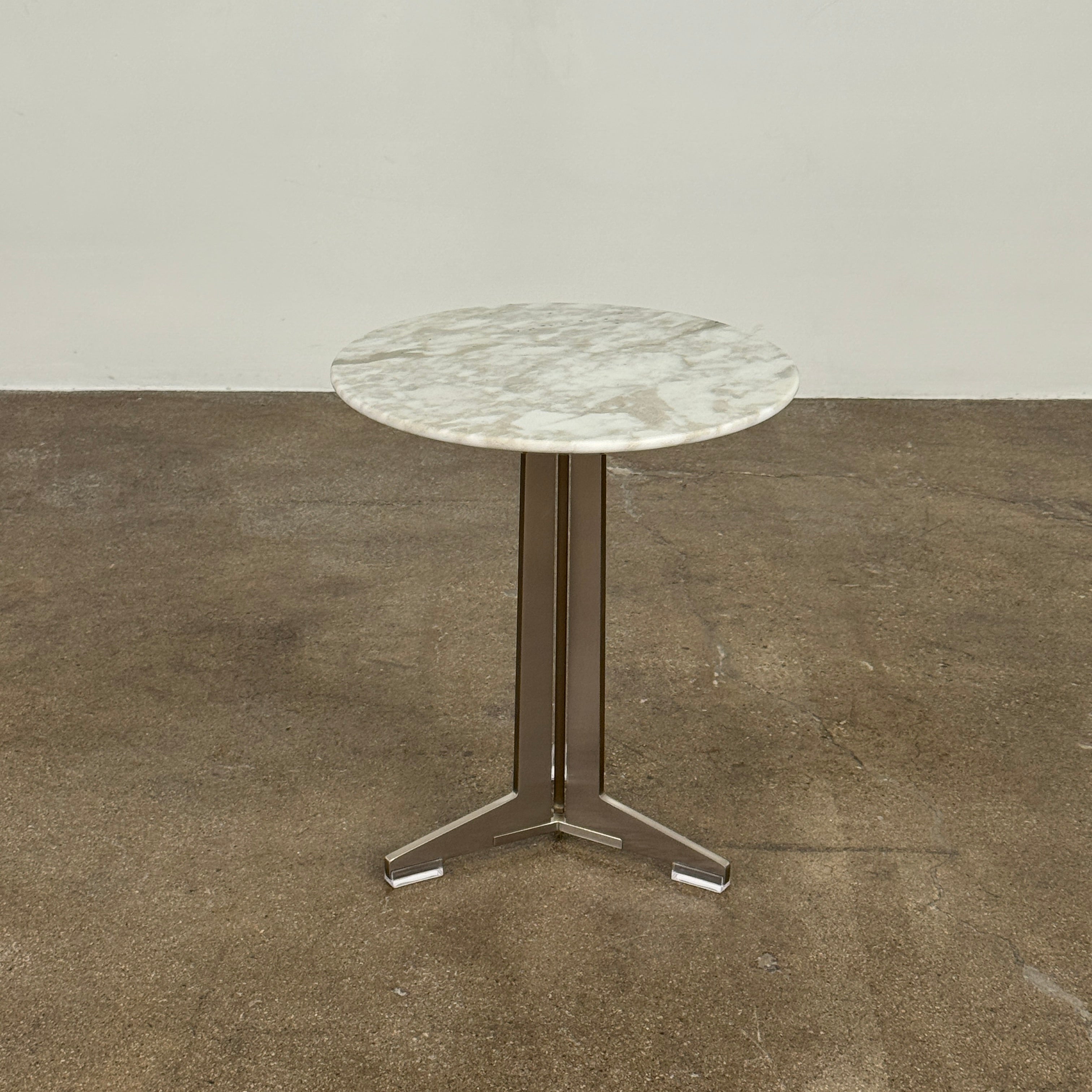 The Flexform Fly Small Table by Modern Resale is a chic side table with a white marble top and metal base, elegantly positioned on a polished concrete floor against a light-colored wall.