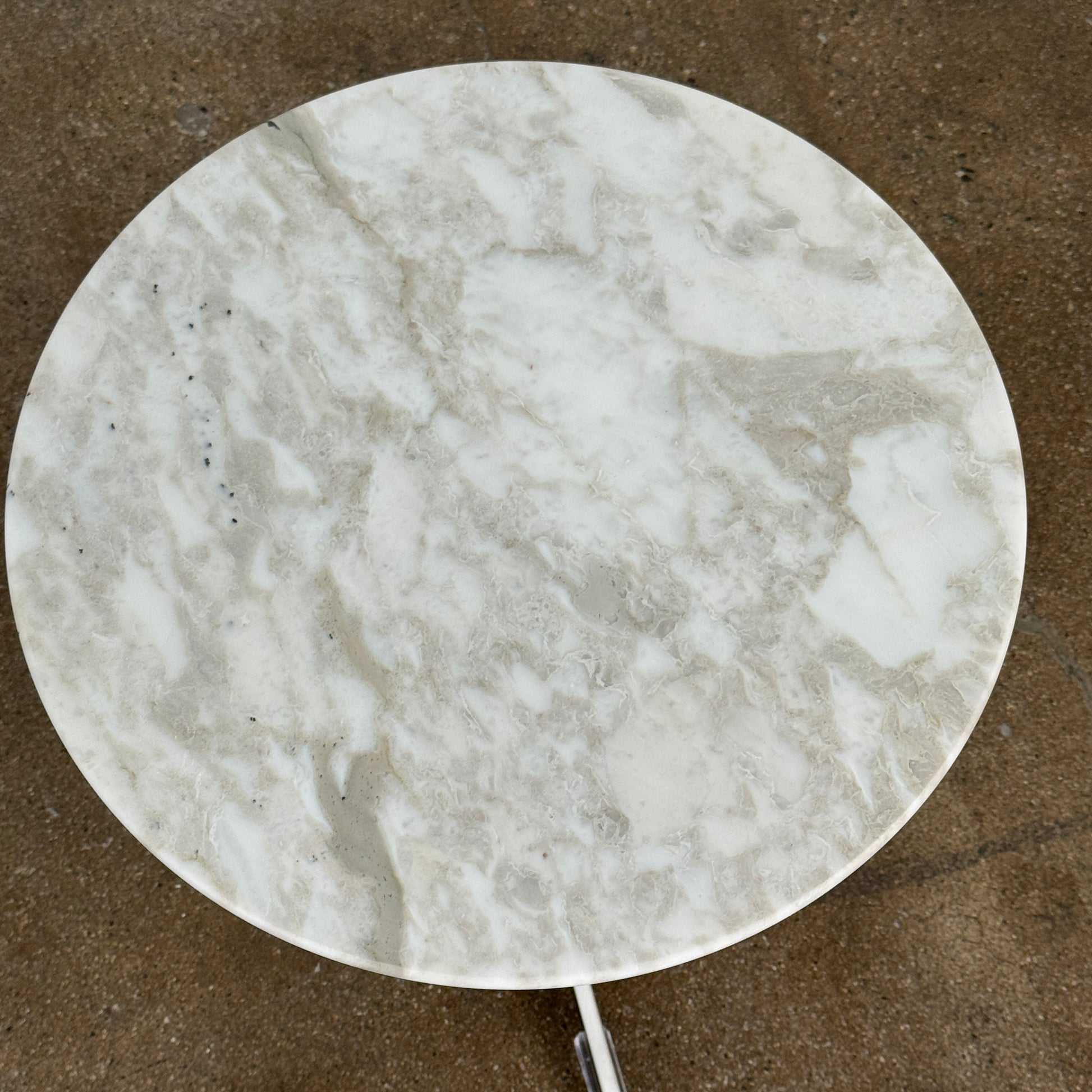 The Flexform Fly Small Table by Modern Resale is a chic side table with a white marble top and metal base, elegantly positioned on a polished concrete floor against a light-colored wall.