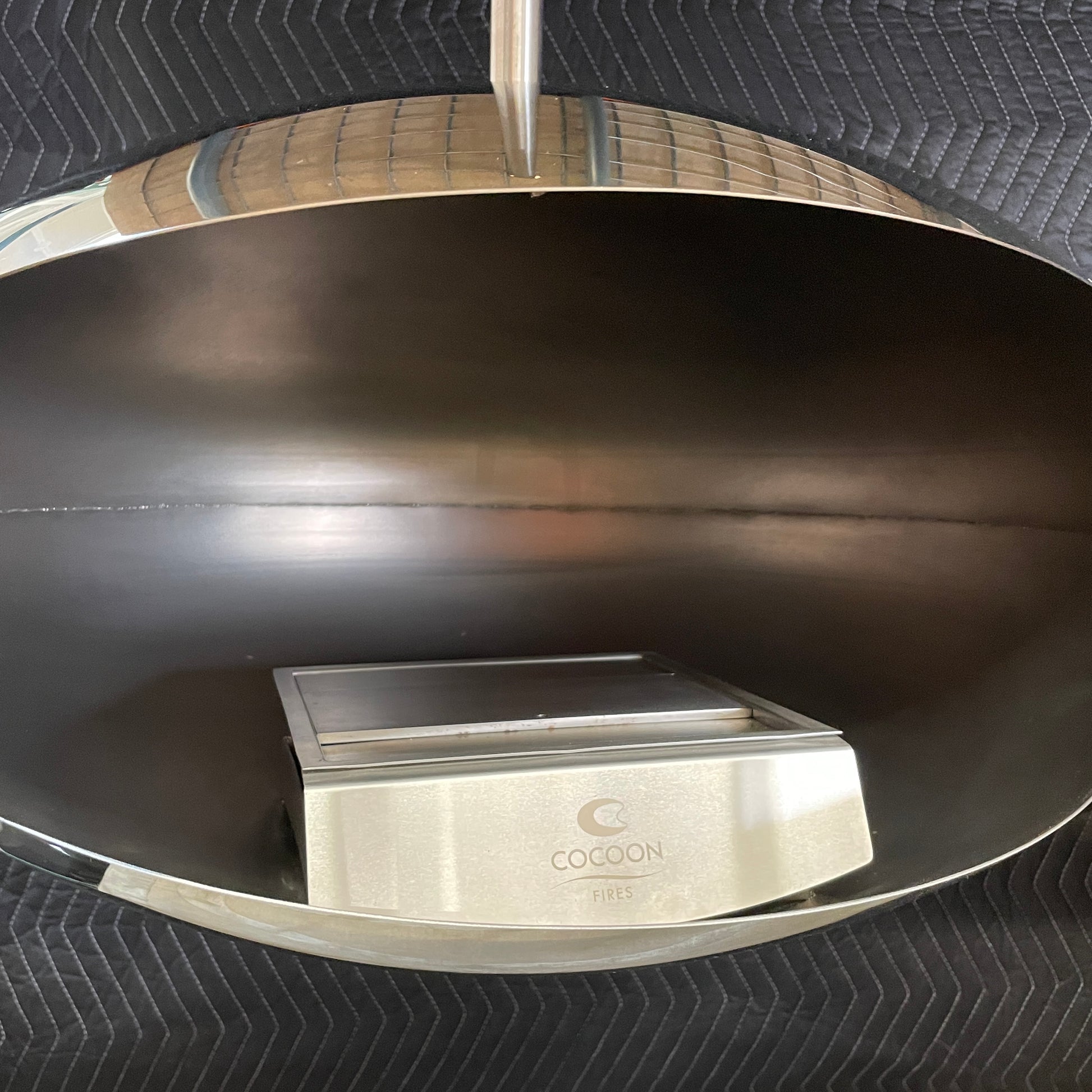 The Plushpod Cocoon Hanging Fireplace is a modern marvel with its oval design, sleek metallic finish, and reflective surface. Its rectangular opening radiates warmth and adds style to any space.