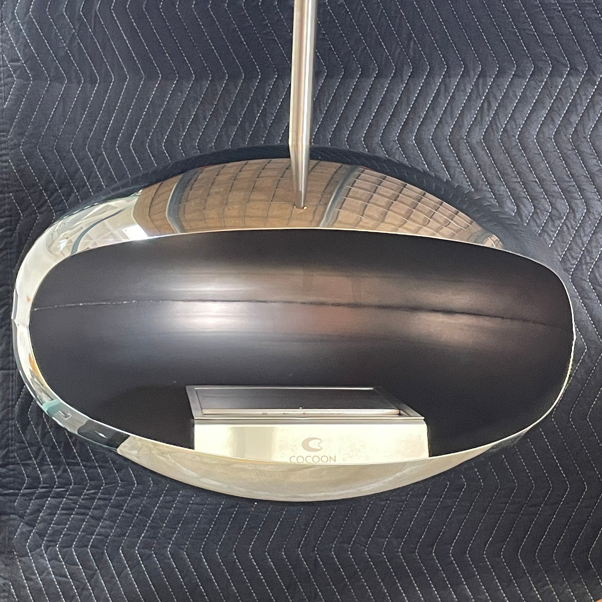 The Plushpod Cocoon Hanging Fireplace is a modern marvel with its oval design, sleek metallic finish, and reflective surface. Its rectangular opening radiates warmth and adds style to any space.