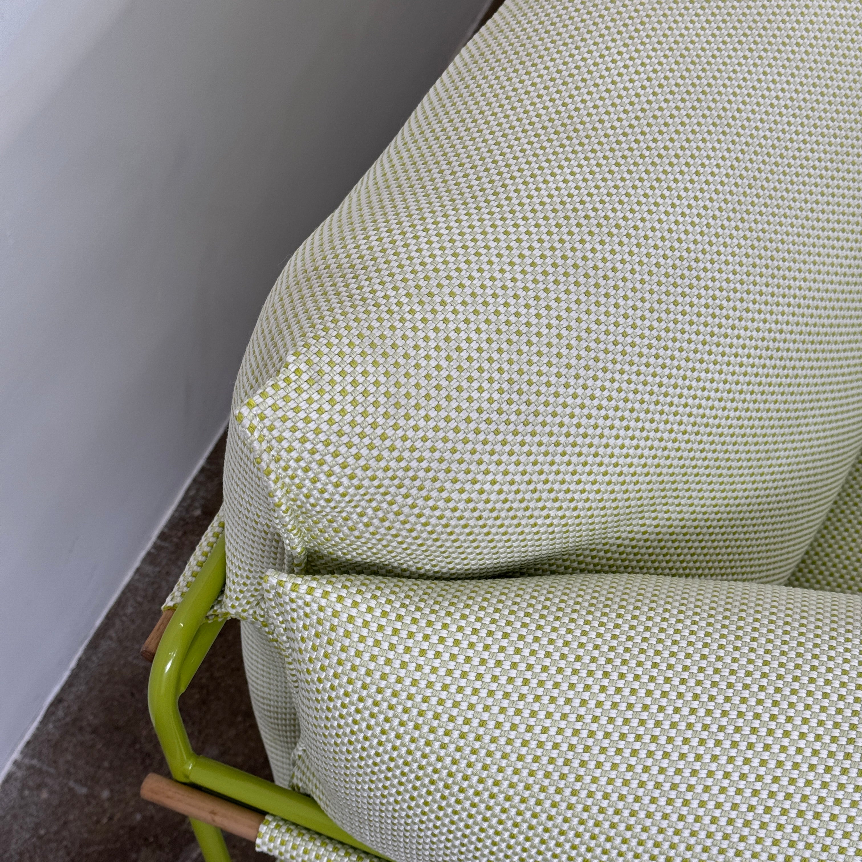 The light green Paola Lenti Kaba Outdoor Sofa by Modern Resale, featuring a metal frame, functions as a stylish two-seater and is shown against a plain white wall on a brown concrete floor.