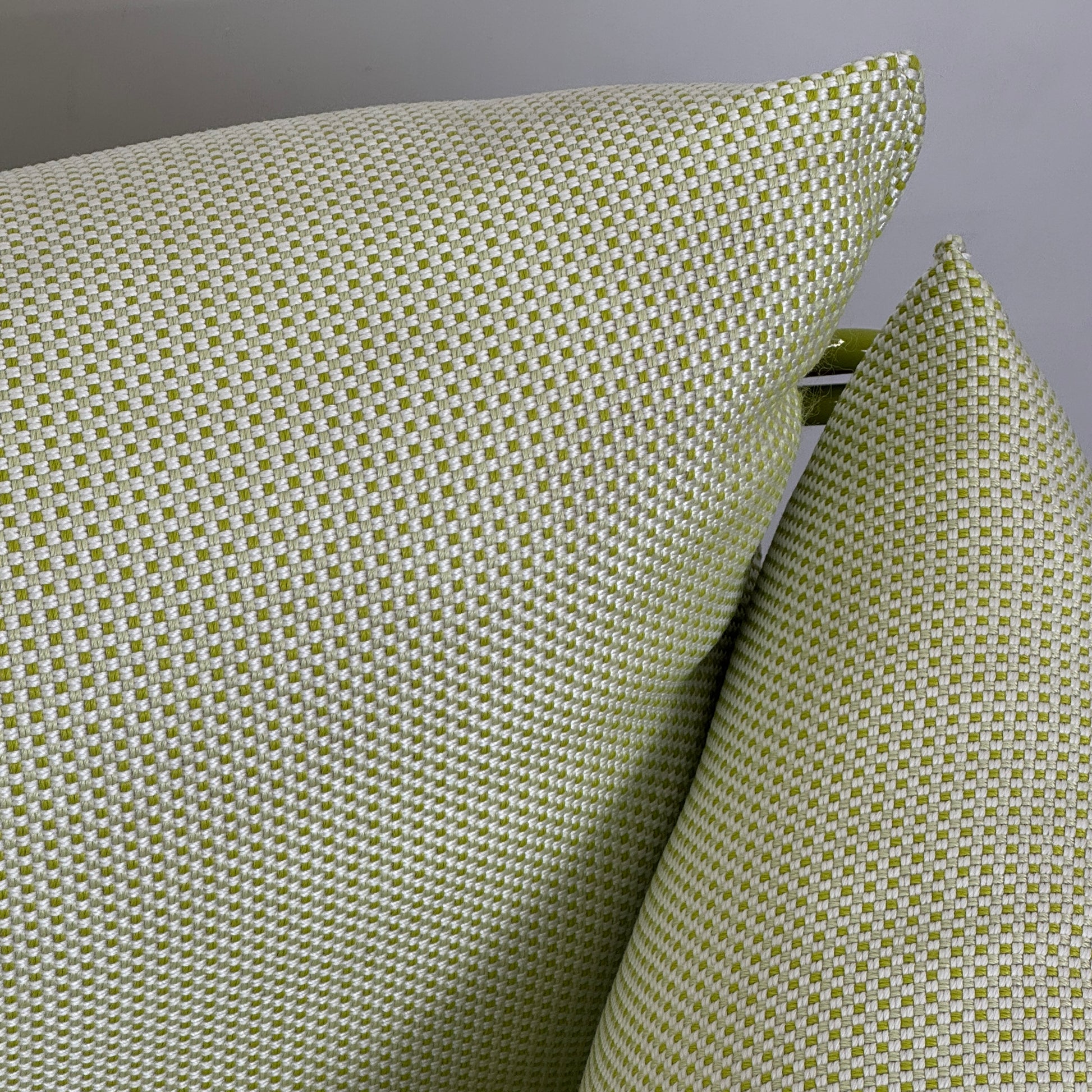 The light green Paola Lenti Kaba Outdoor Sofa by Modern Resale, featuring a metal frame, functions as a stylish two-seater and is shown against a plain white wall on a brown concrete floor.