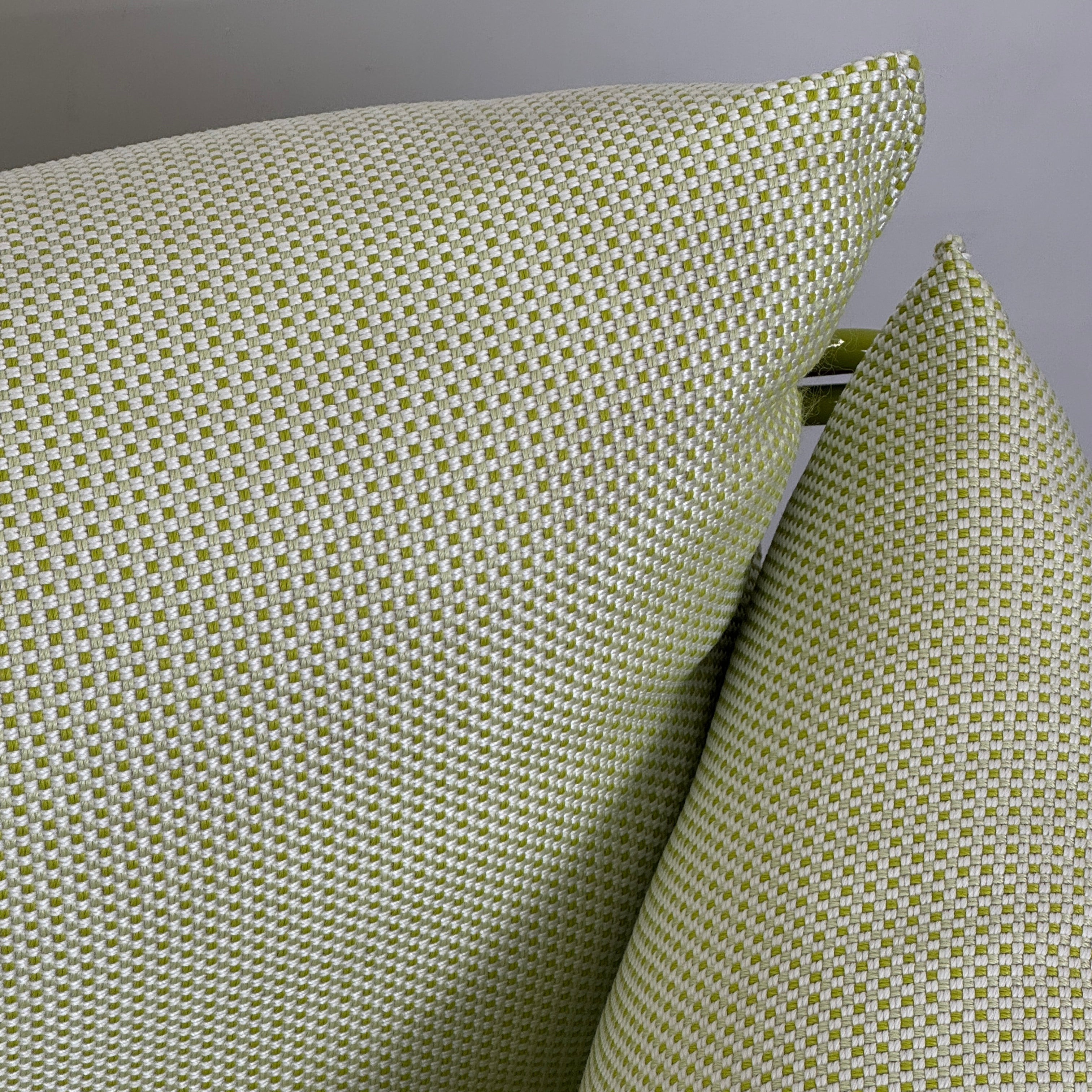 The light green Paola Lenti Kaba Outdoor Sofa by Modern Resale, featuring a metal frame, functions as a stylish two-seater and is shown against a plain white wall on a brown concrete floor.