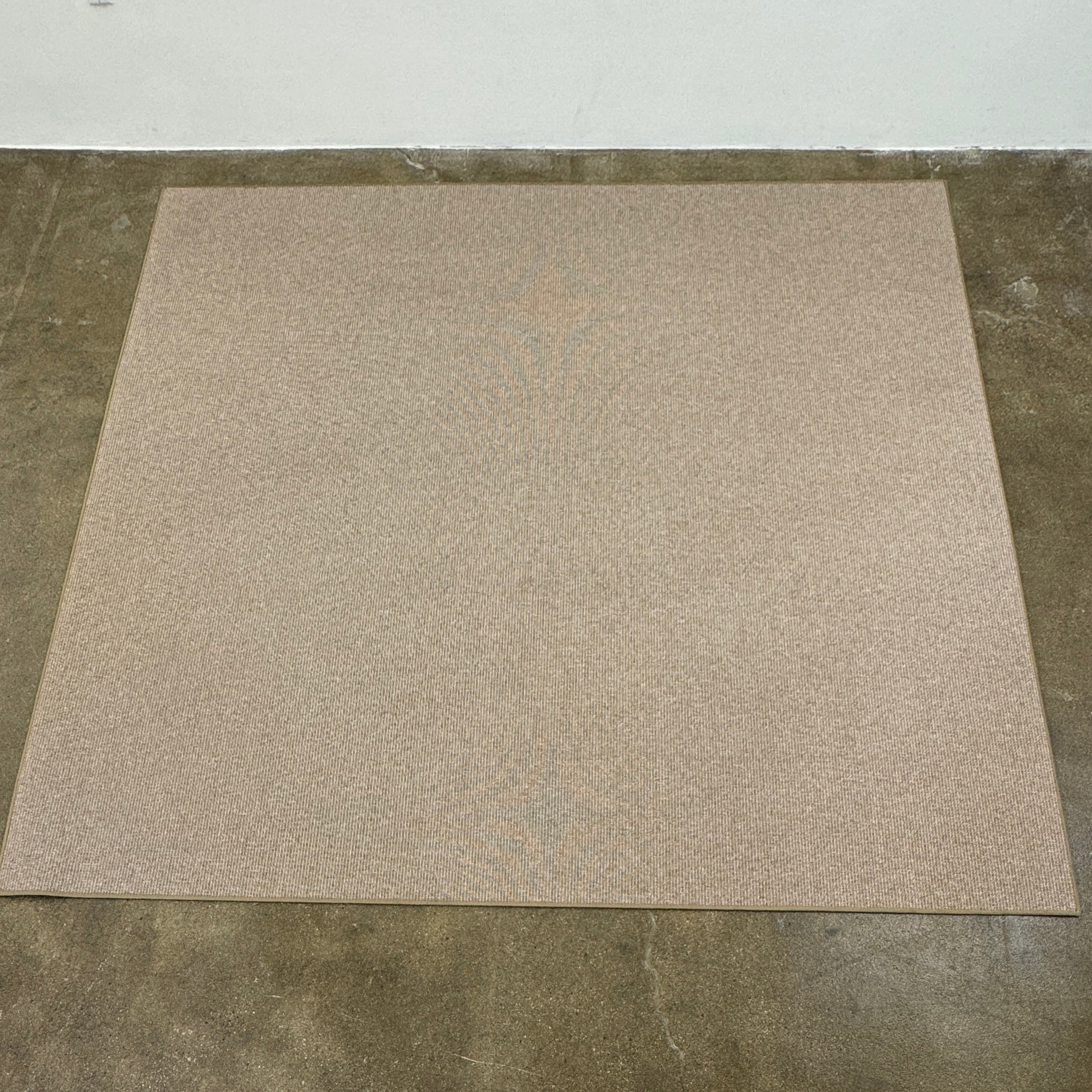 A beige Flexform Paride Rug with stitched edges rests on a polished concrete floor.