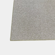 A beige Flexform Paride Rug with stitched edges rests on a polished concrete floor.