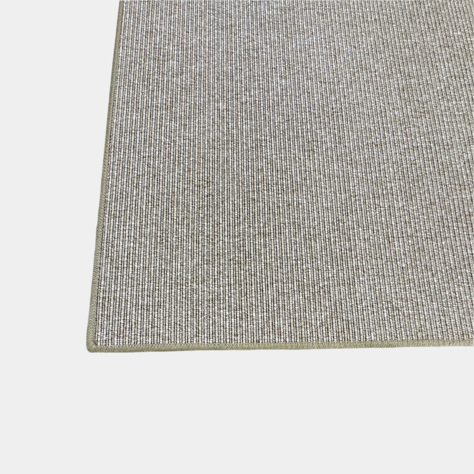 A beige Flexform Paride Rug with stitched edges rests on a polished concrete floor.