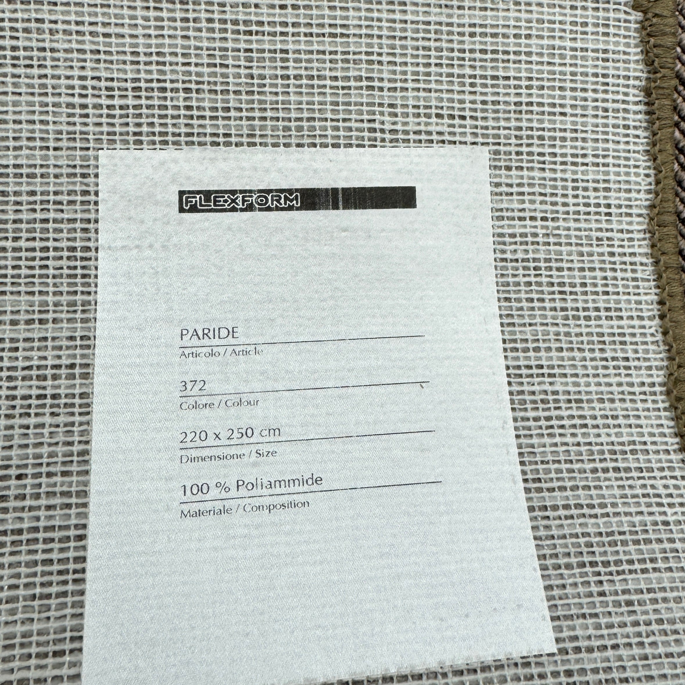 A beige Flexform Paride Rug with stitched edges rests on a polished concrete floor.