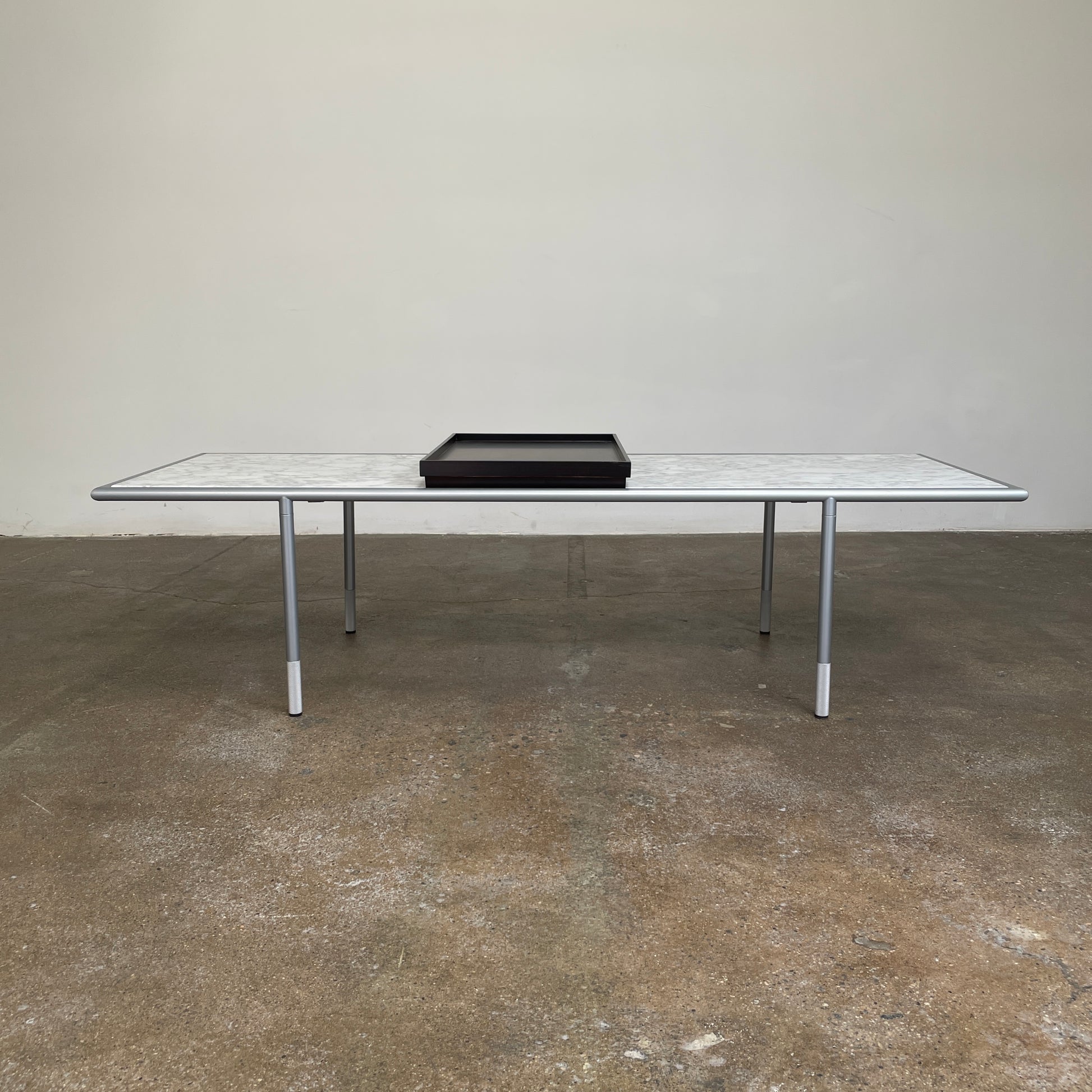 The Artelano Carrara Marble Coffee Table boasts a rectangular marble top with sleek metal legs and a central wood tray, exuding the Parisian elegance of the Artelano brand.