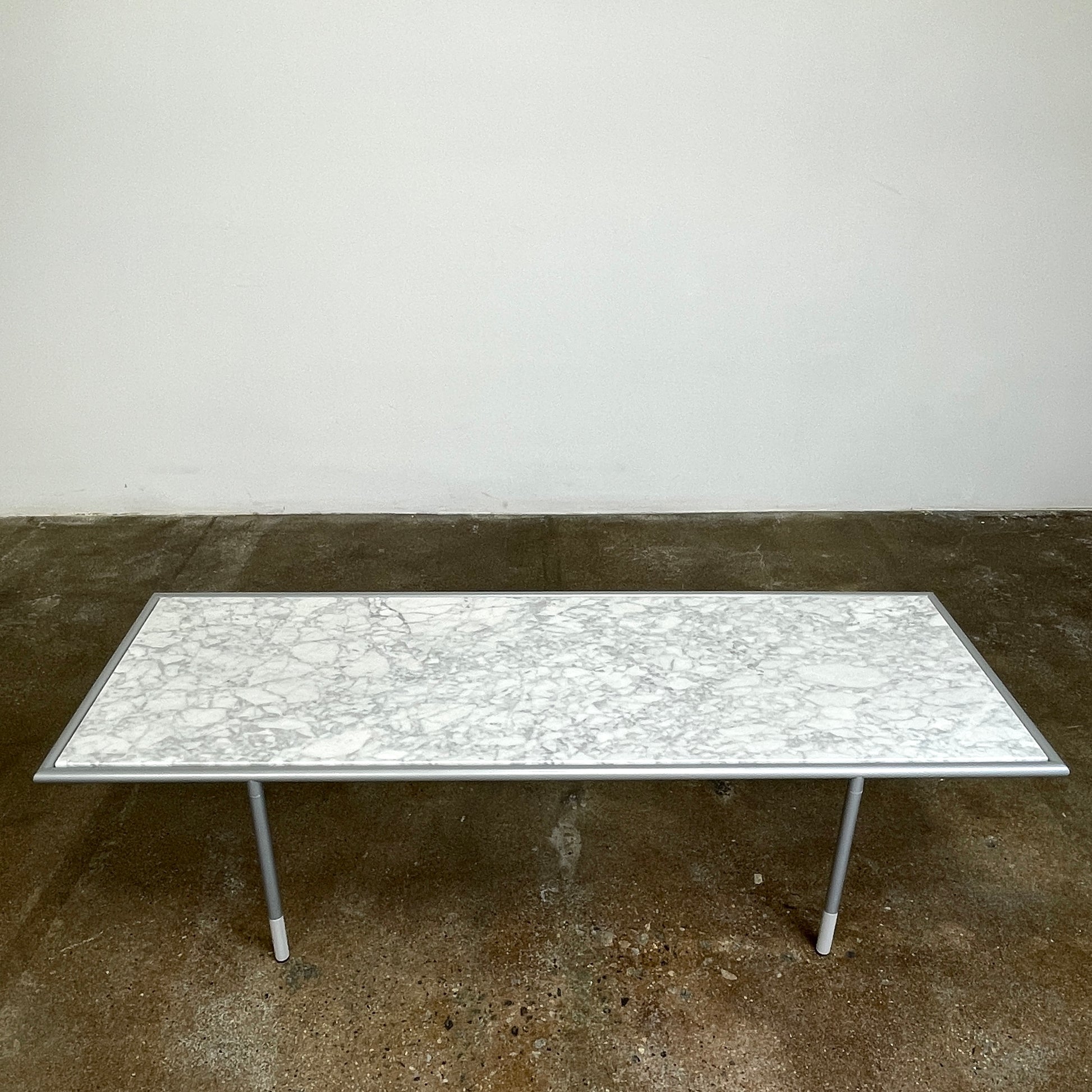 The Artelano Carrara Marble Coffee Table boasts a rectangular marble top with sleek metal legs and a central wood tray, exuding the Parisian elegance of the Artelano brand.