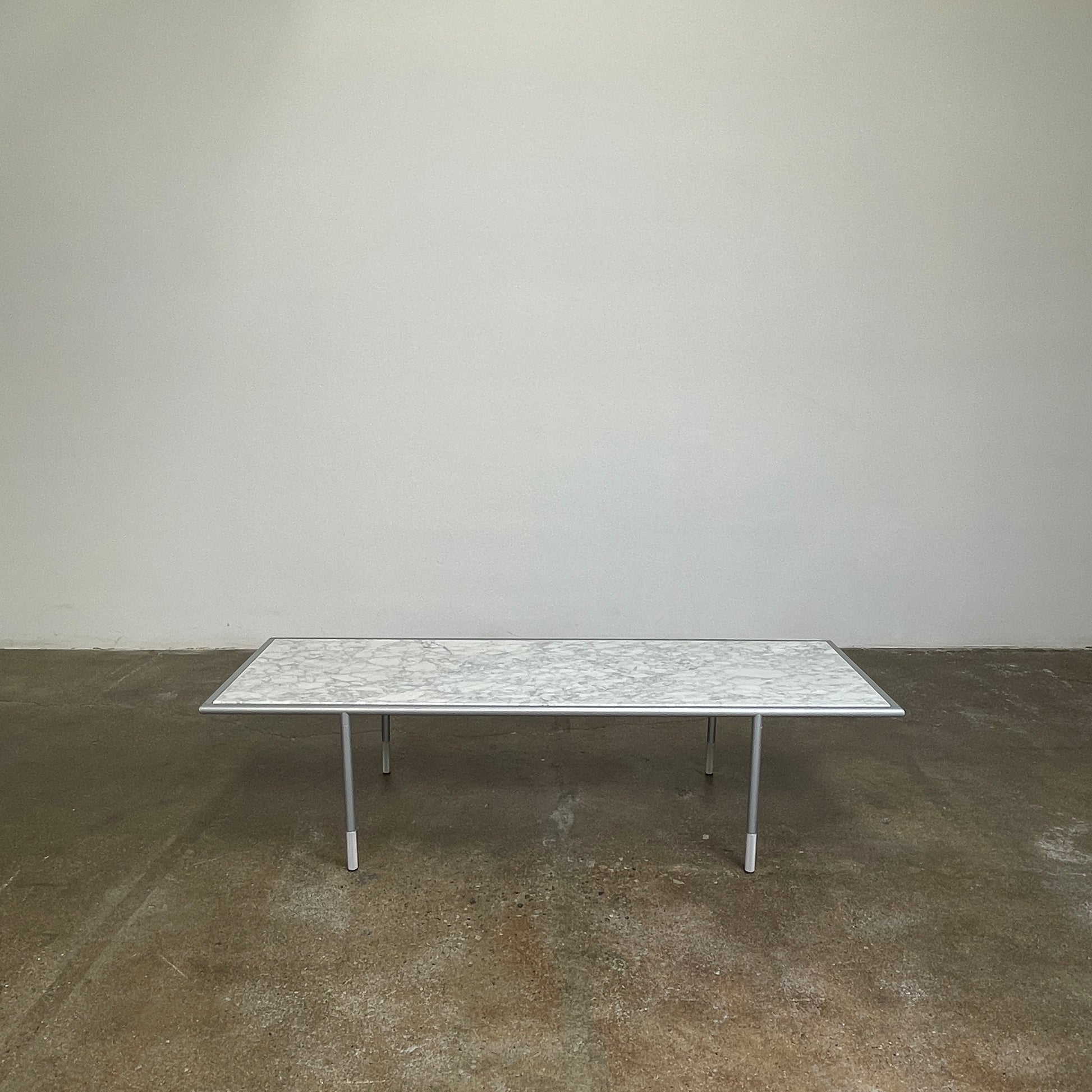 The Artelano Carrara Marble Coffee Table boasts a rectangular marble top with sleek metal legs and a central wood tray, exuding the Parisian elegance of the Artelano brand.