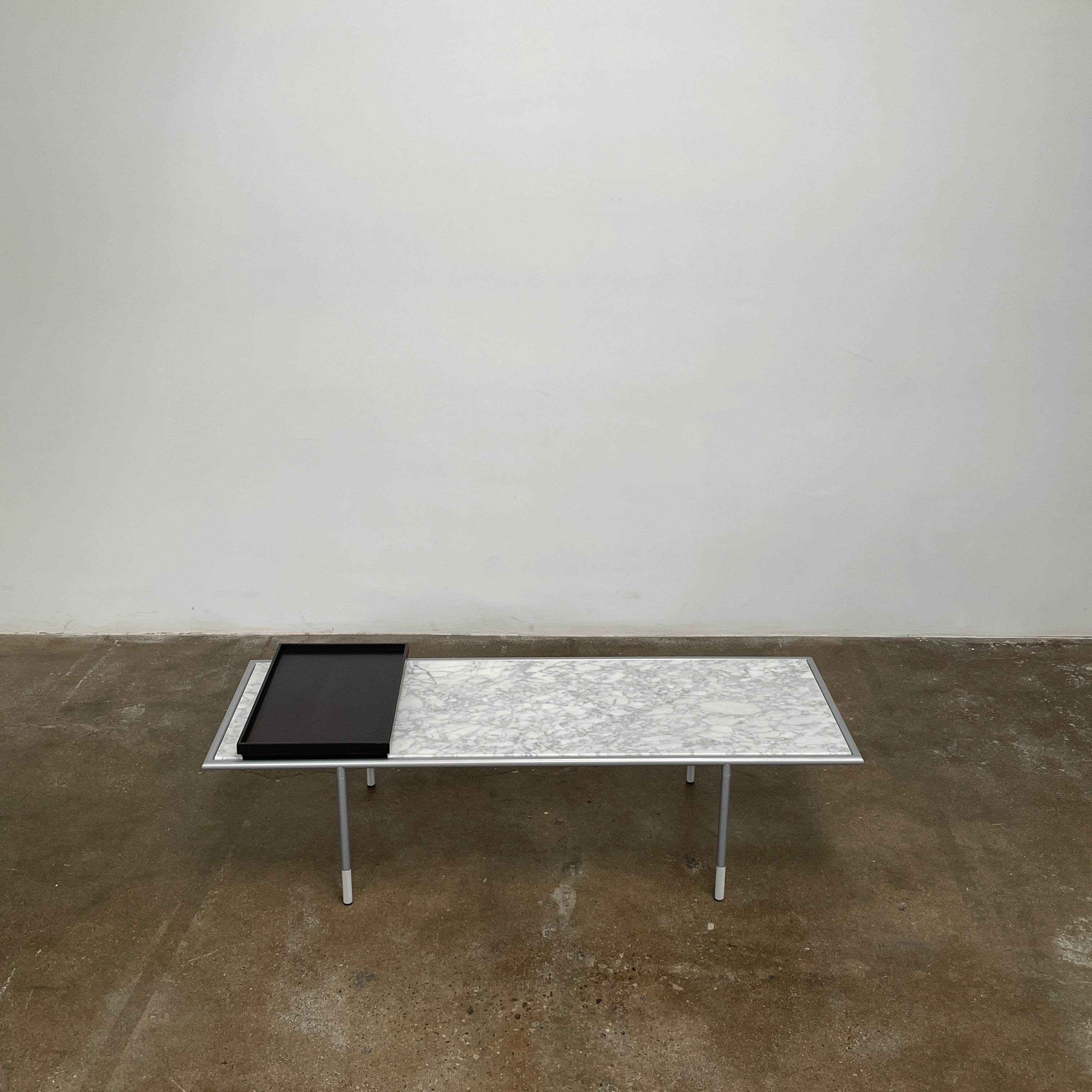 The Artelano Carrara Marble Coffee Table boasts a rectangular marble top with sleek metal legs and a central wood tray, exuding the Parisian elegance of the Artelano brand.
