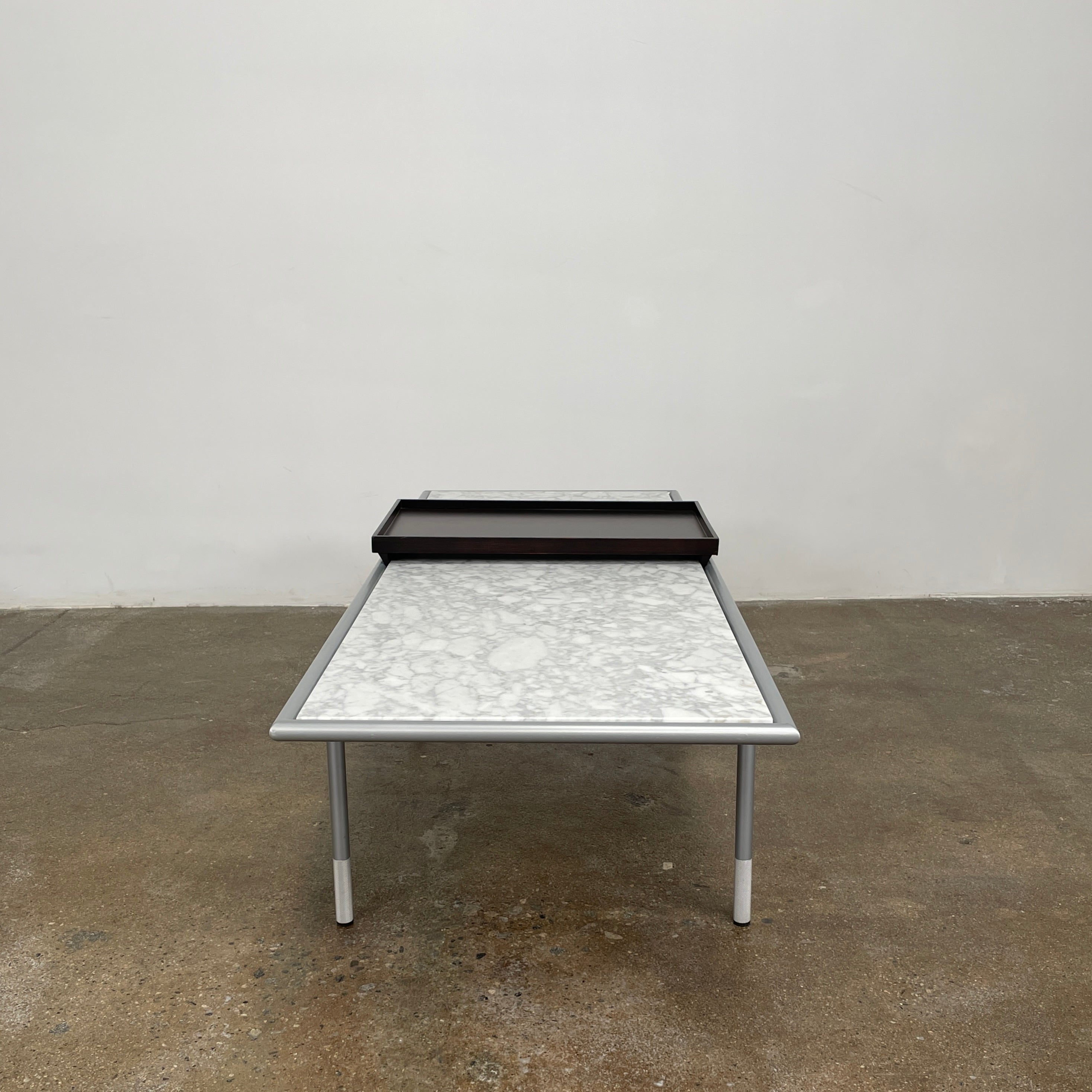 The Artelano Carrara Marble Coffee Table boasts a rectangular marble top with sleek metal legs and a central wood tray, exuding the Parisian elegance of the Artelano brand.