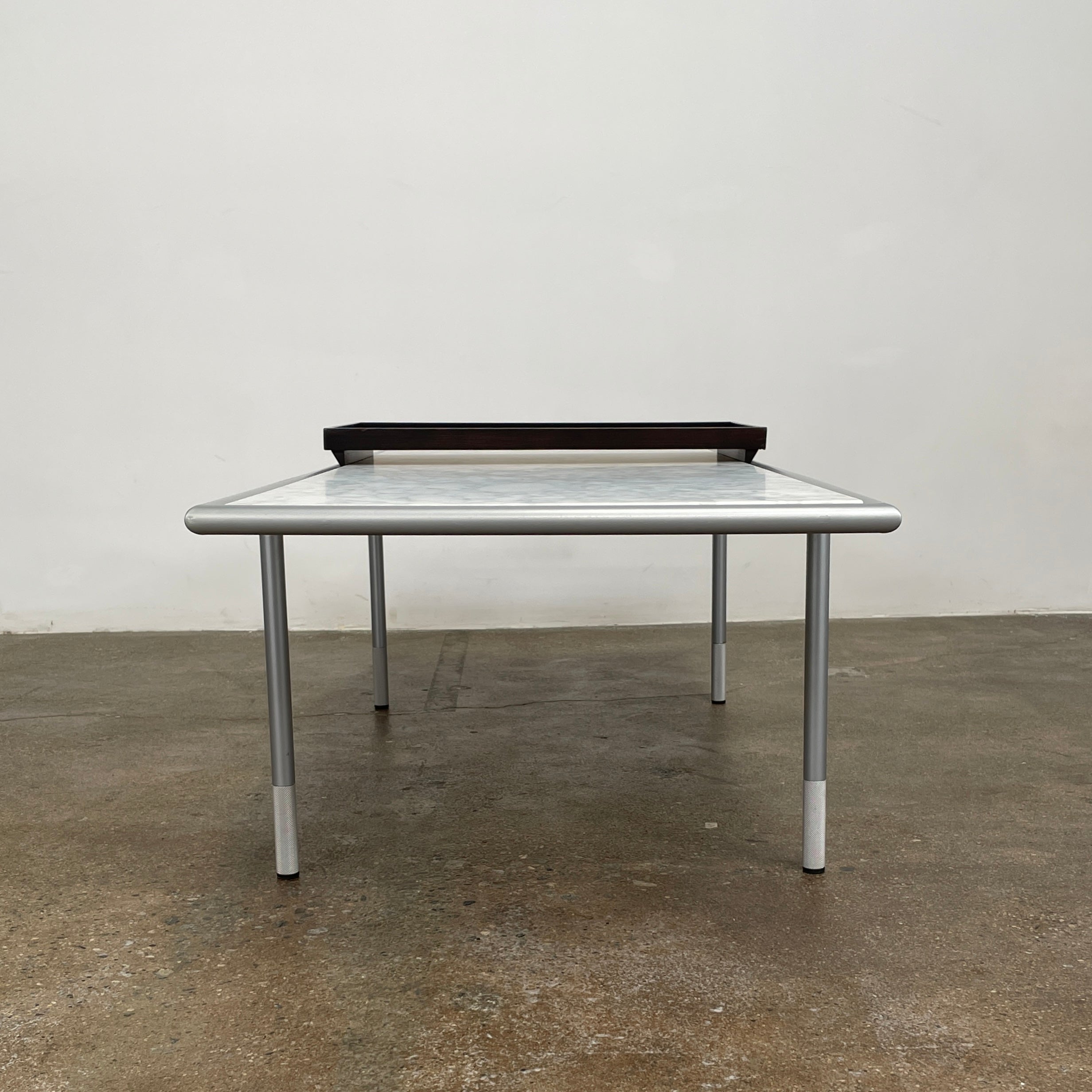 The Artelano Carrara Marble Coffee Table boasts a rectangular marble top with sleek metal legs and a central wood tray, exuding the Parisian elegance of the Artelano brand.