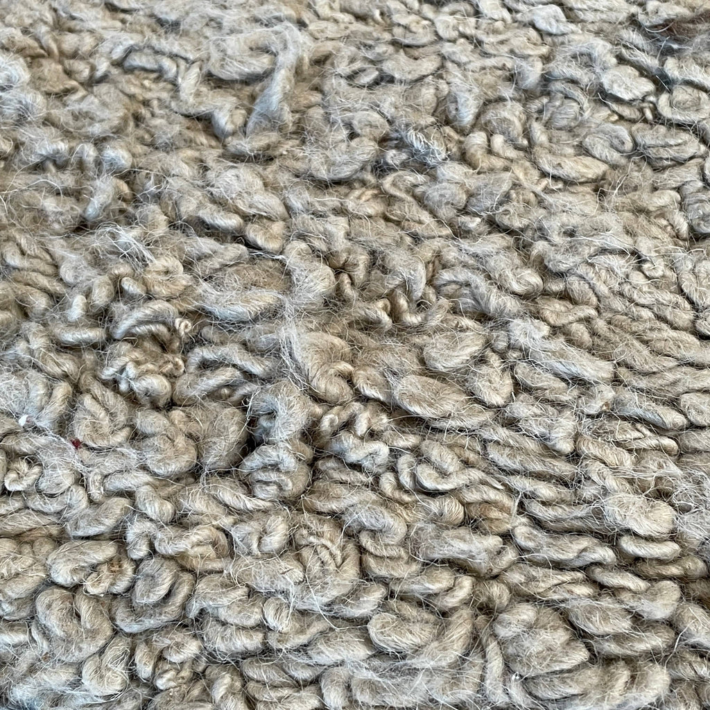 Close-up of a textured Delinear Anemone Looped Un-Dyed 8'X10' Wool Rug (hold) with a folded corner.