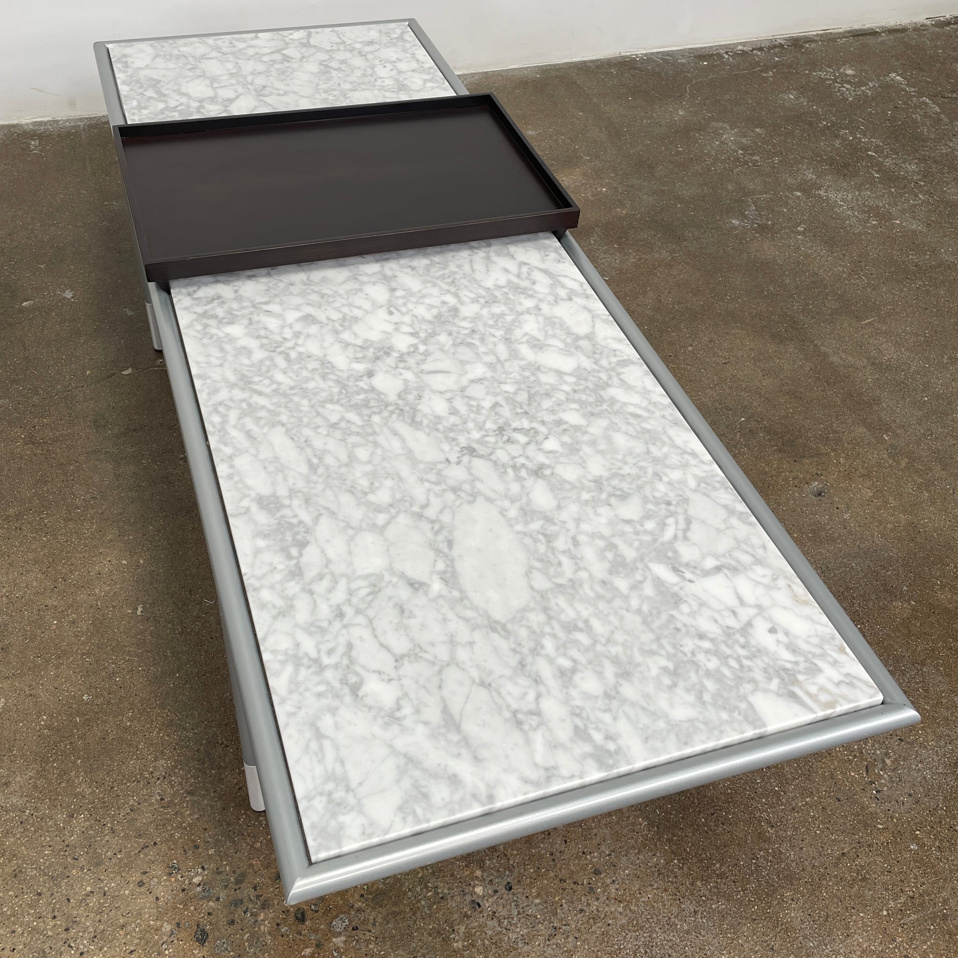 The Artelano Carrara Marble Coffee Table boasts a rectangular marble top with sleek metal legs and a central wood tray, exuding the Parisian elegance of the Artelano brand.