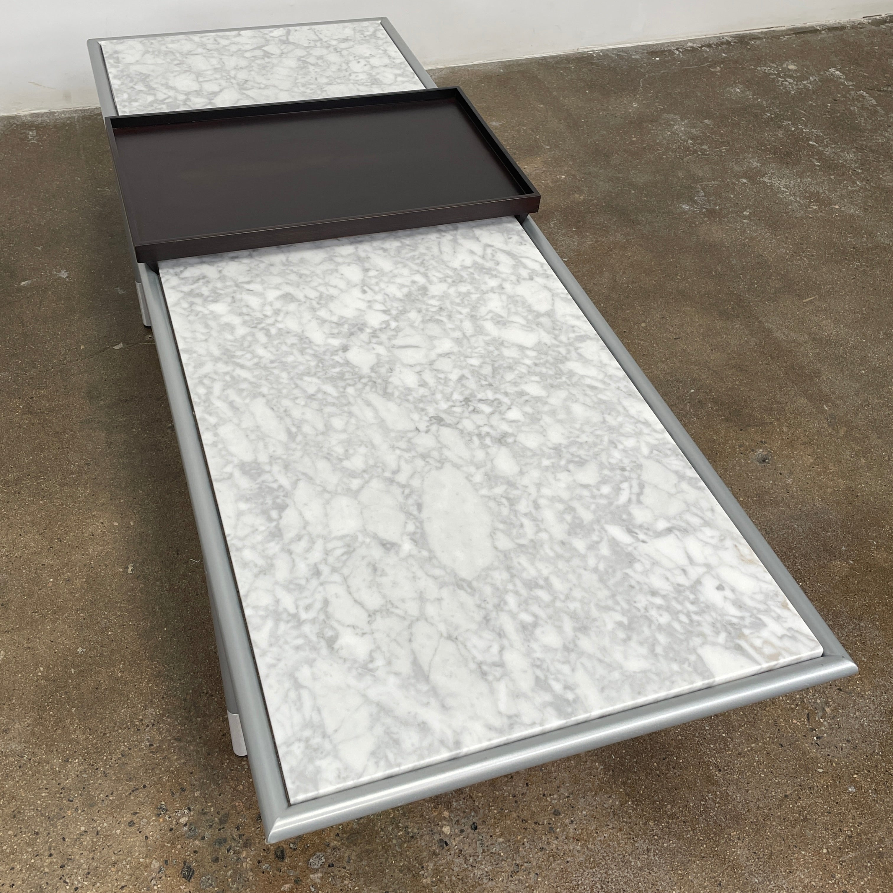 The Artelano Carrara Marble Coffee Table boasts a rectangular marble top with sleek metal legs and a central wood tray, exuding the Parisian elegance of the Artelano brand.