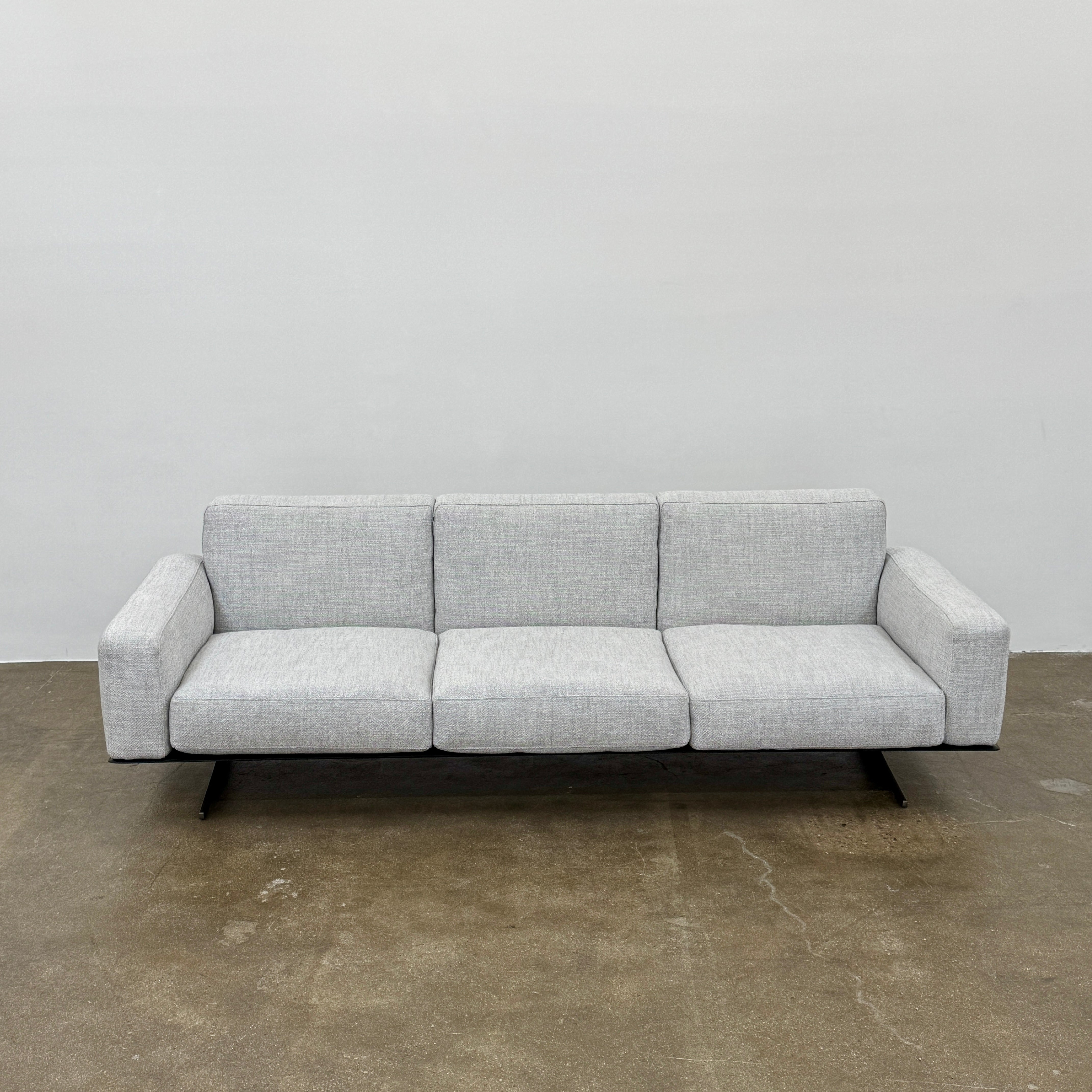 A contemporary Flexform Dream Sofa in light gray, featuring wide armrests and black metal legs, is displayed against a plain white background.