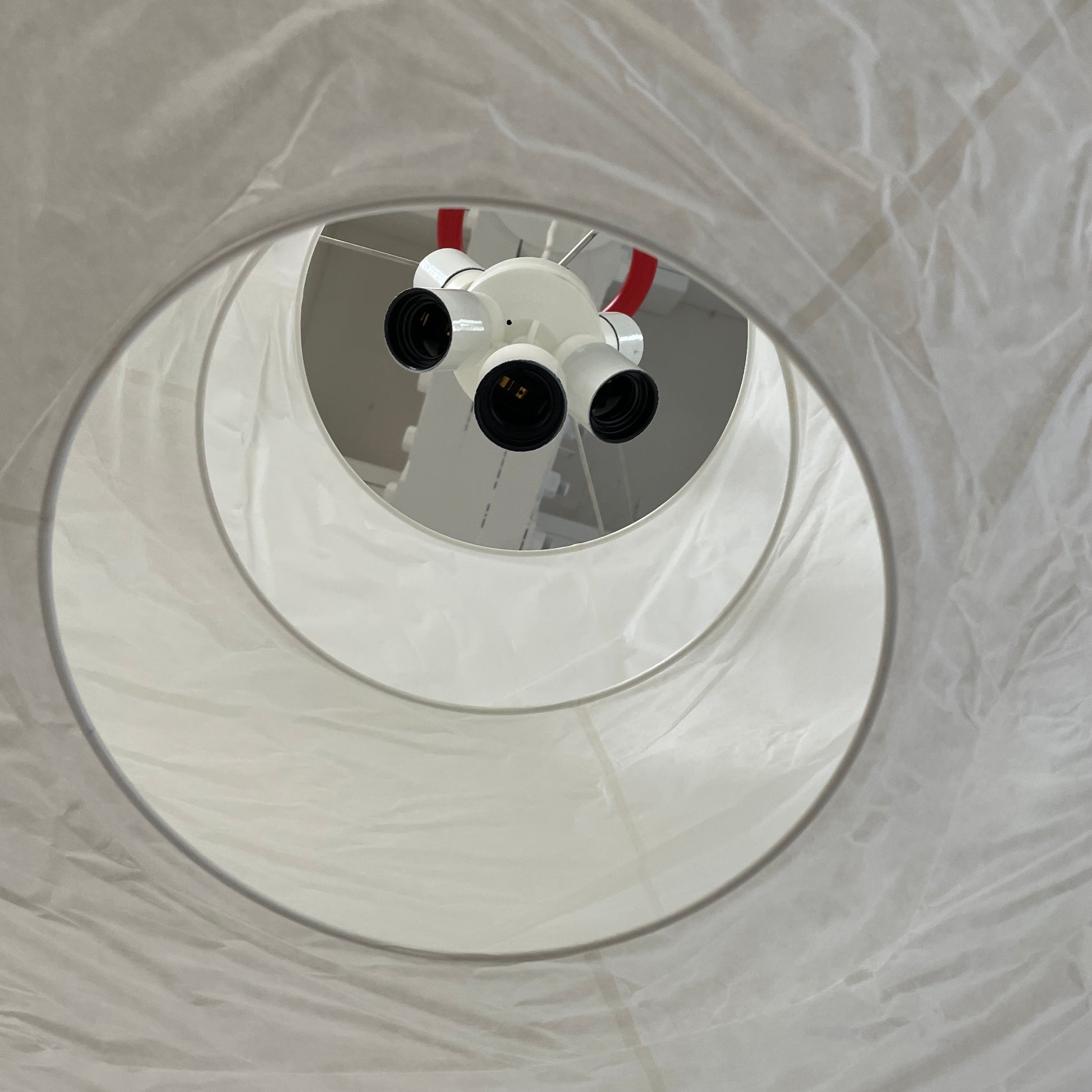 The Ingo Maurer Floatation Suspension Light Medium Size is a modern chandelier with a red ring accent and three overlapping circular discs, showcasing Ingo Maurer's artistry with its elegant and innovative design, suspended elegantly by wires.