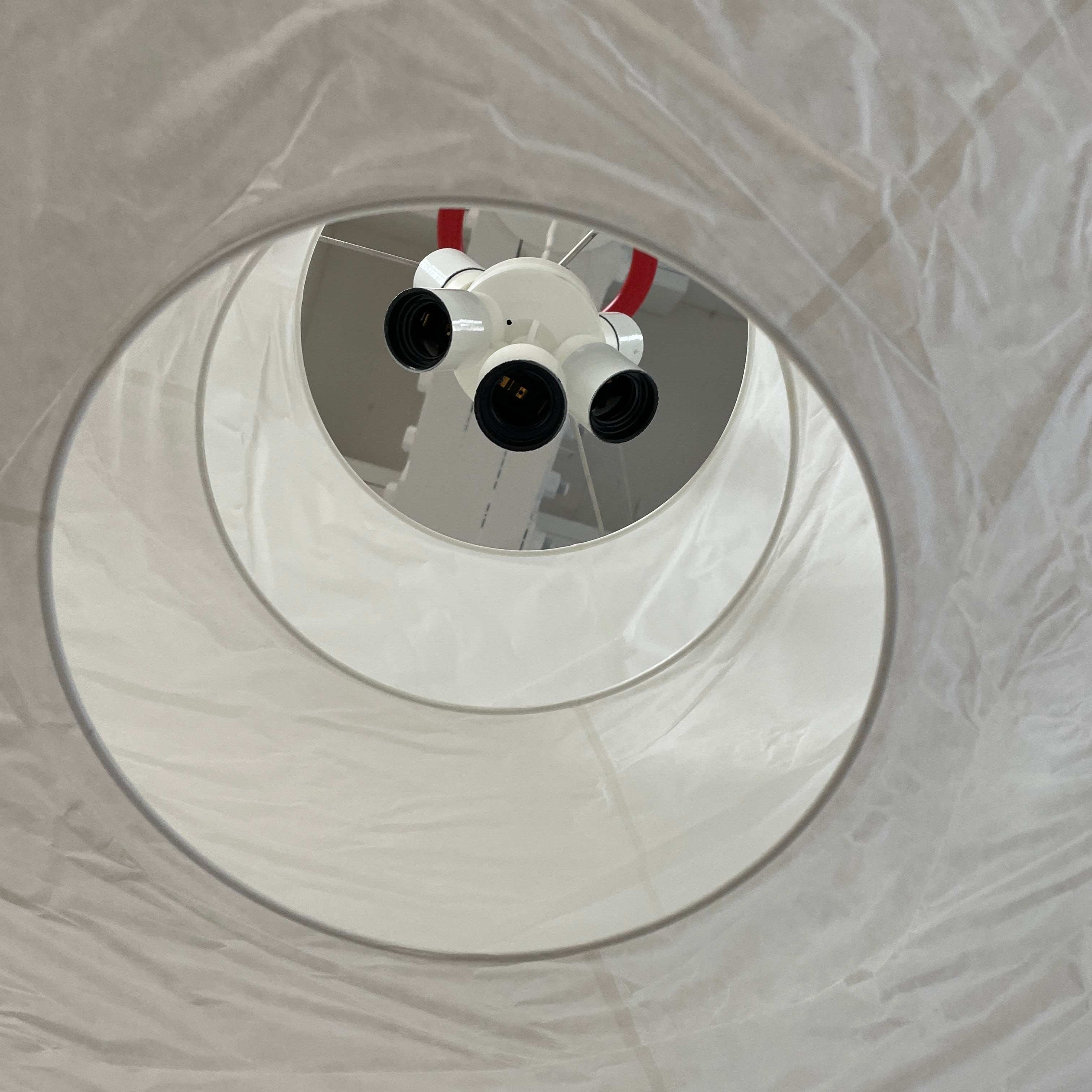 The Ingo Maurer Floatation Suspension Light Medium Size is a modern chandelier with a red ring accent and three overlapping circular discs, showcasing Ingo Maurer's artistry with its elegant and innovative design, suspended elegantly by wires.