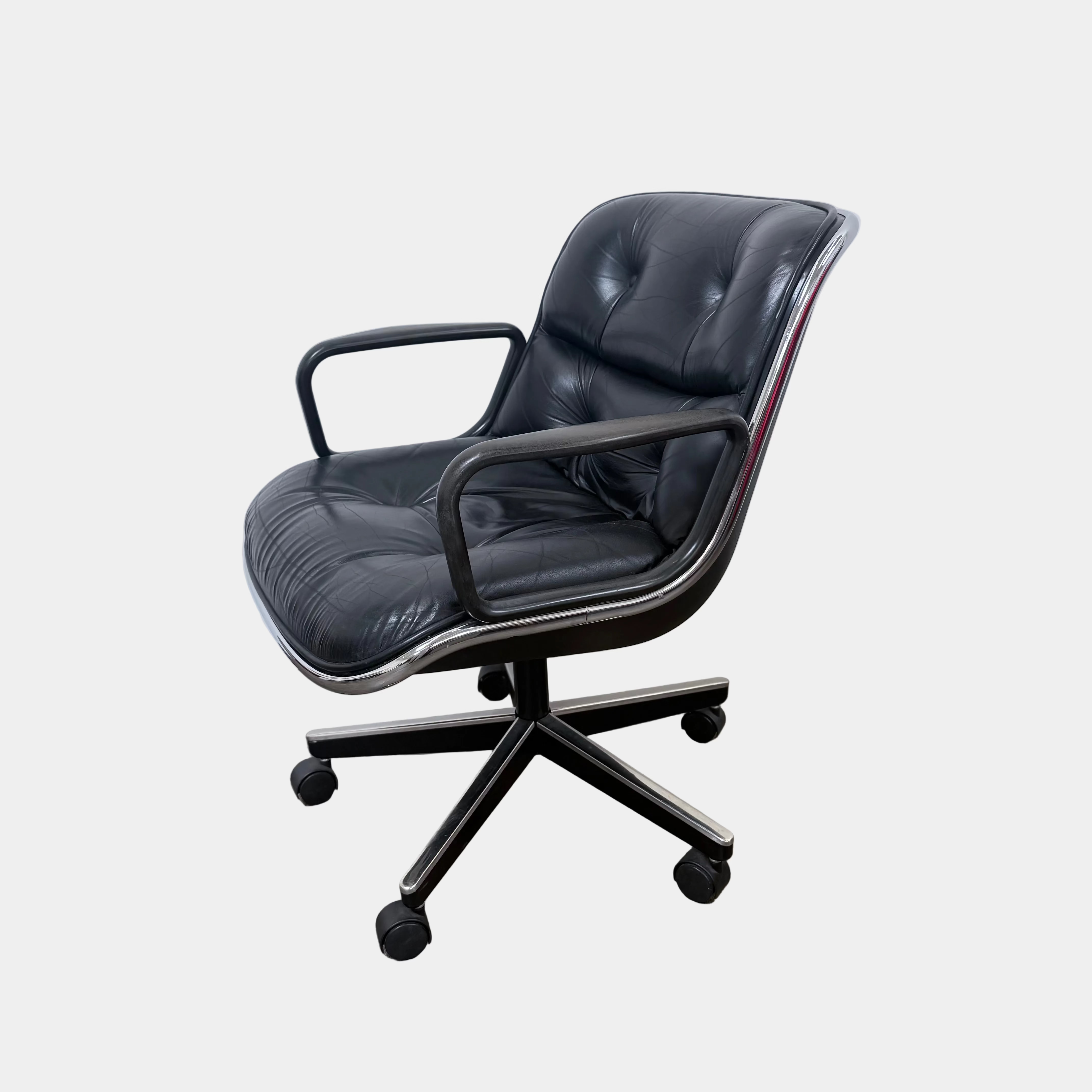 A DWR Pollock Executive Chair with a chrome frame and five wheels is shown from the back, set on a concrete floor against a plain white wall.