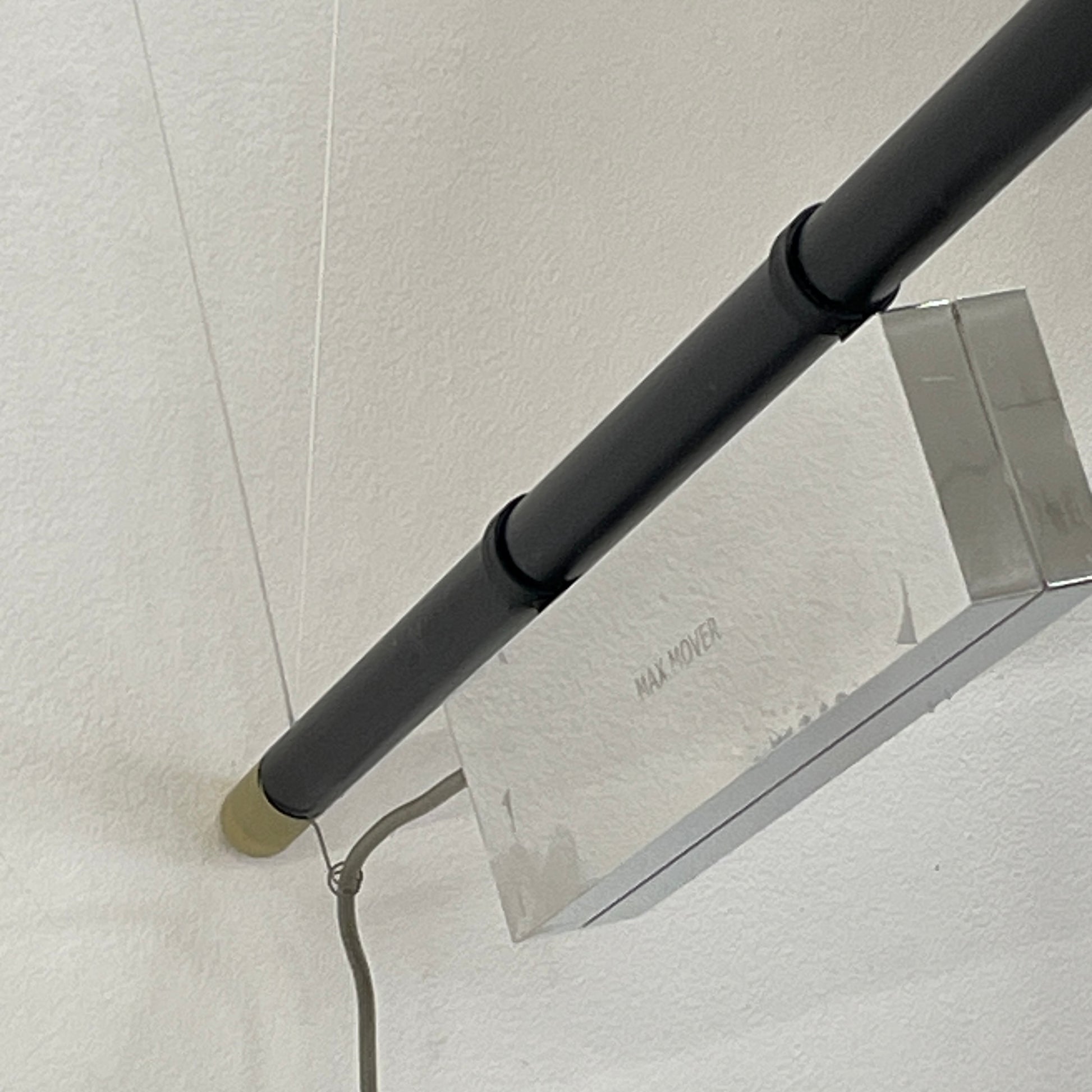 The Ingo Maurer Max Mover Wall Light by Ingo Maurer is a contemporary fixture with an adjustable telescopic rod, sleek black arm, and aluminum reflector in a dome-shaped shade set against a light grey backdrop.