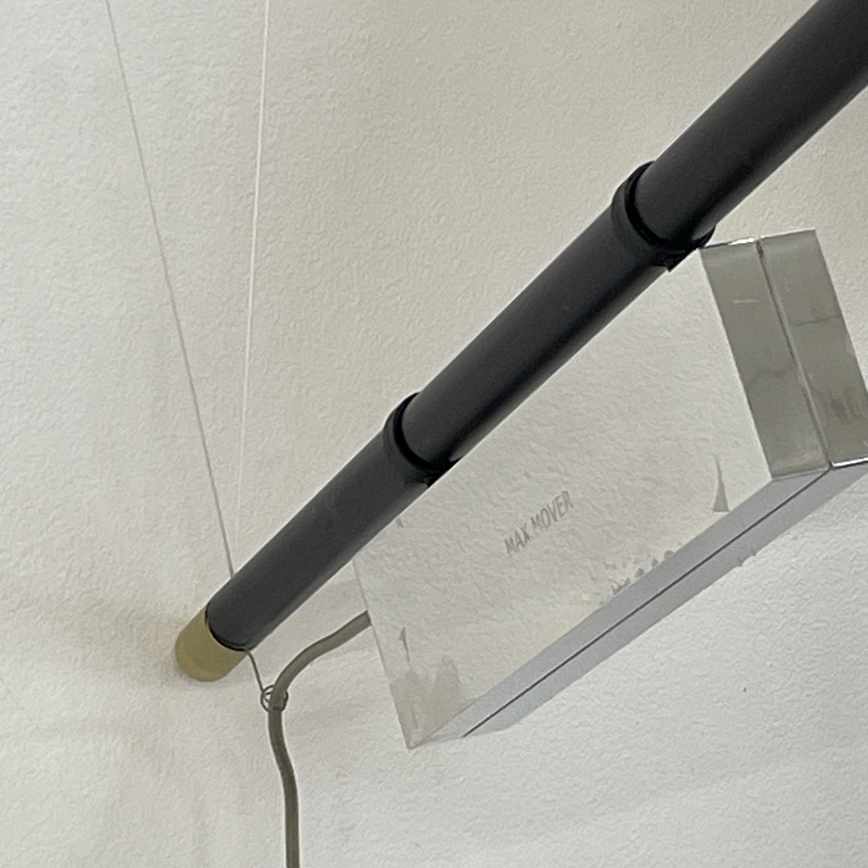 The Ingo Maurer Max Mover Wall Light by Ingo Maurer is a contemporary fixture with an adjustable telescopic rod, sleek black arm, and aluminum reflector in a dome-shaped shade set against a light grey backdrop.