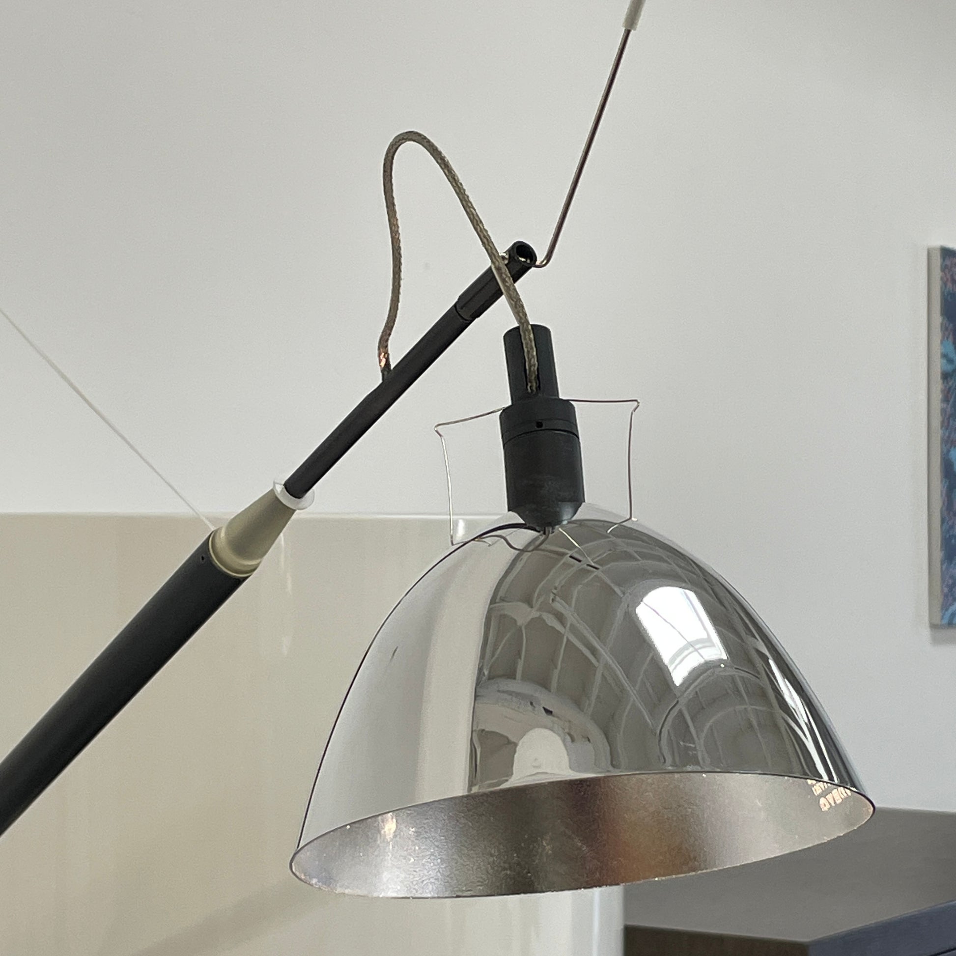The Ingo Maurer Max Mover Wall Light by Ingo Maurer is a contemporary fixture with an adjustable telescopic rod, sleek black arm, and aluminum reflector in a dome-shaped shade set against a light grey backdrop.