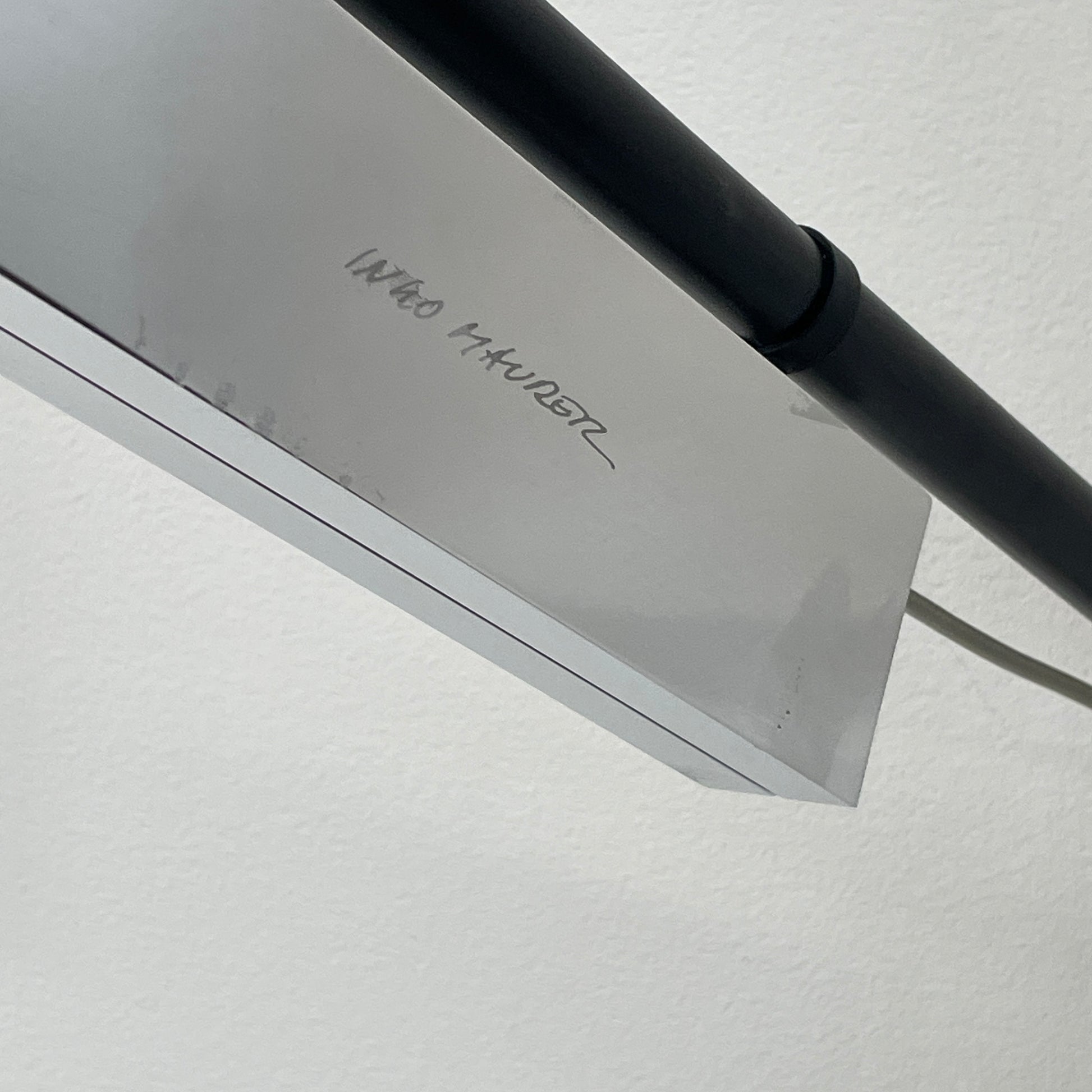 The Ingo Maurer Max Mover Wall Light by Ingo Maurer is a contemporary fixture with an adjustable telescopic rod, sleek black arm, and aluminum reflector in a dome-shaped shade set against a light grey backdrop.