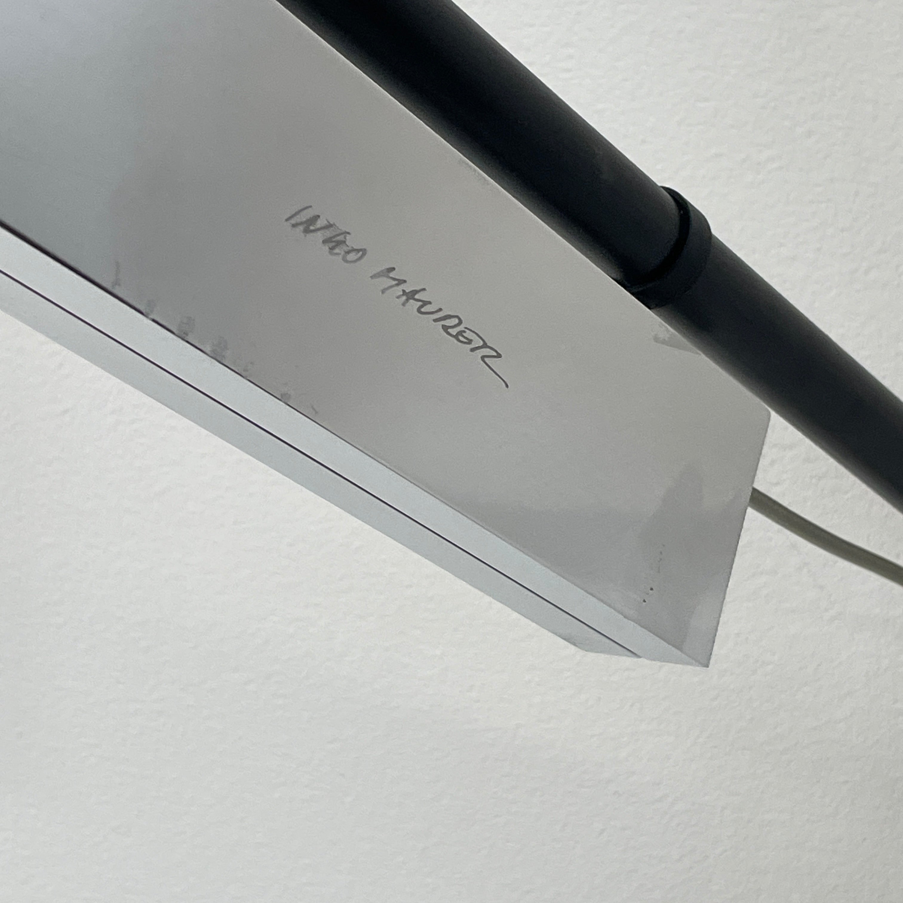 The Ingo Maurer Max Mover Wall Light by Ingo Maurer is a contemporary fixture with an adjustable telescopic rod, sleek black arm, and aluminum reflector in a dome-shaped shade set against a light grey backdrop.