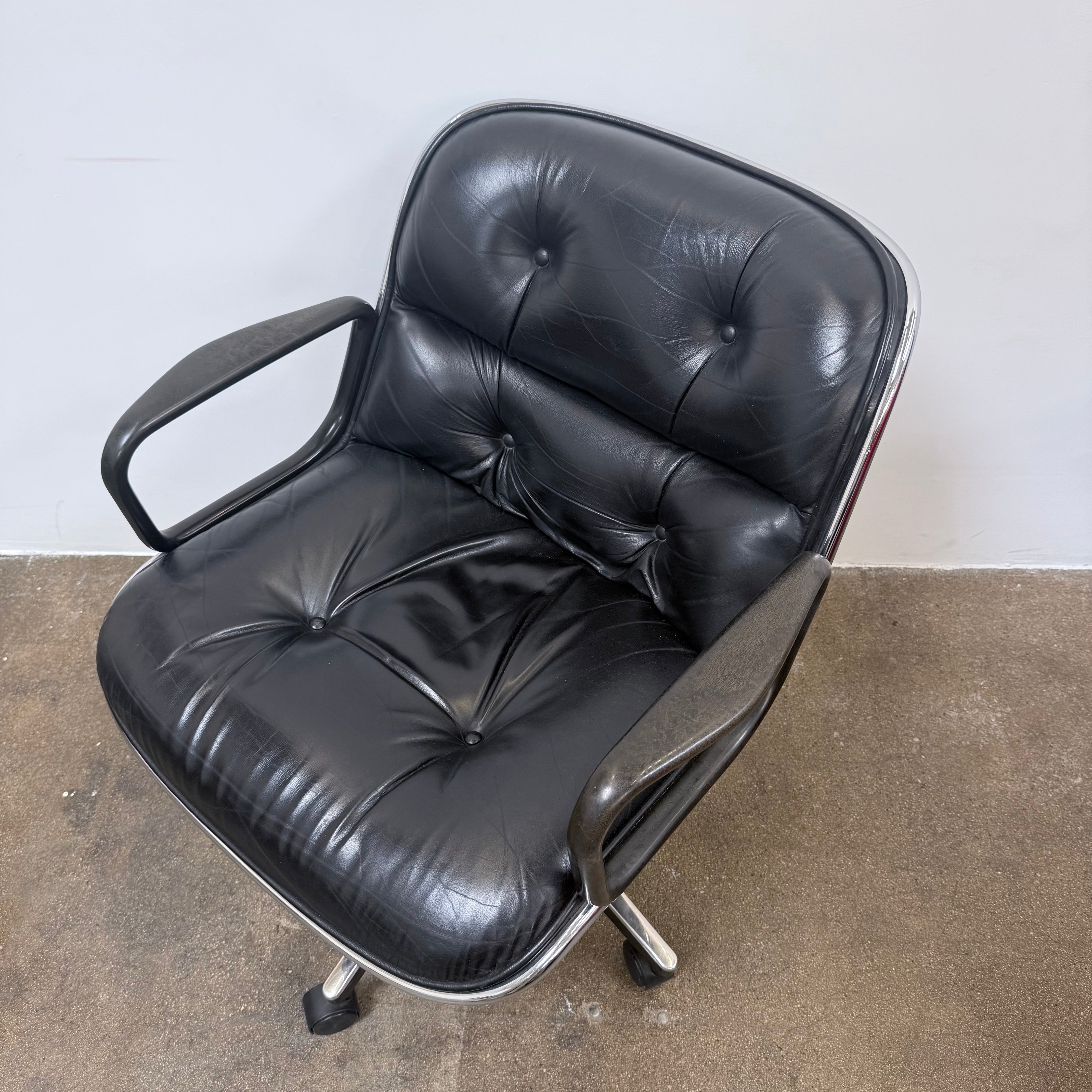 A DWR Pollock Executive Chair with a chrome frame and five wheels is shown from the back, set on a concrete floor against a plain white wall.