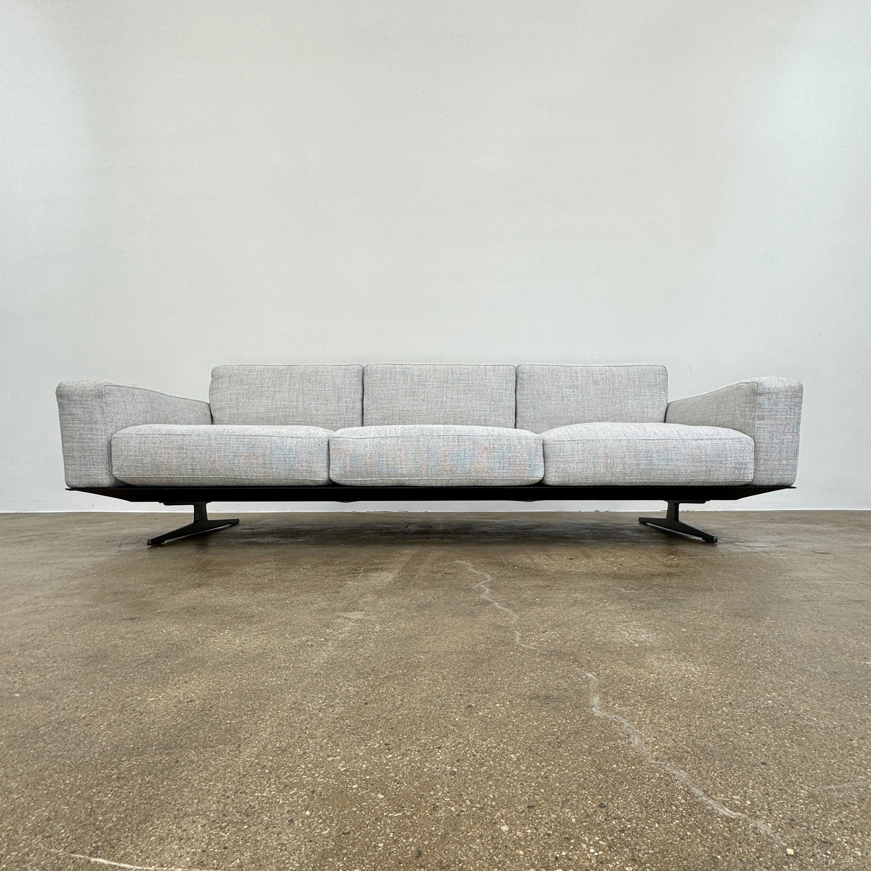 A contemporary Flexform Dream Sofa in light gray, featuring wide armrests and black metal legs, is displayed against a plain white background.