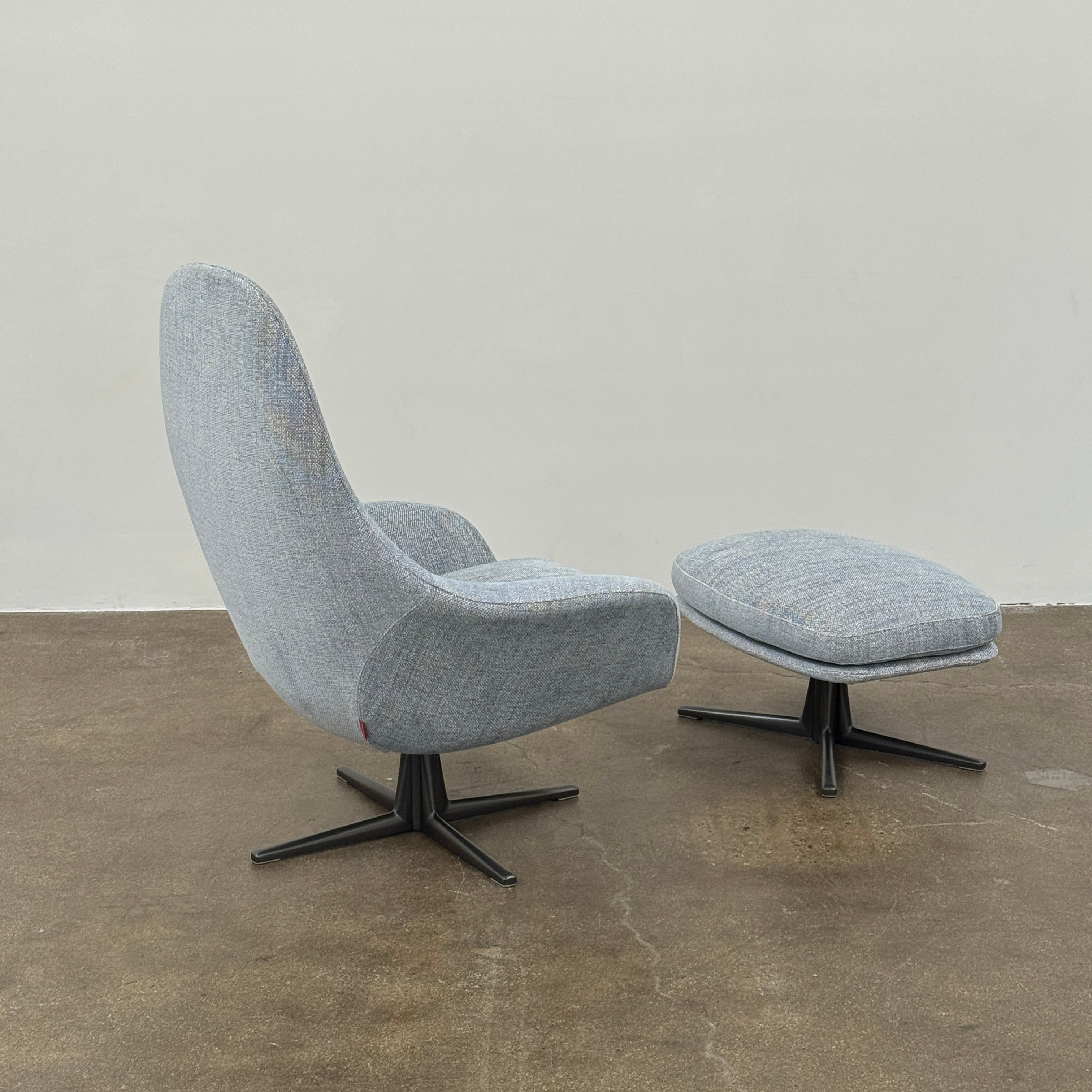 The Flexform Marlon Swivel Armchair and Ottoman, available with two covers, feature ergonomic design and black metal bases from Flexform, shown here in a modern gray finish against a plain white background.