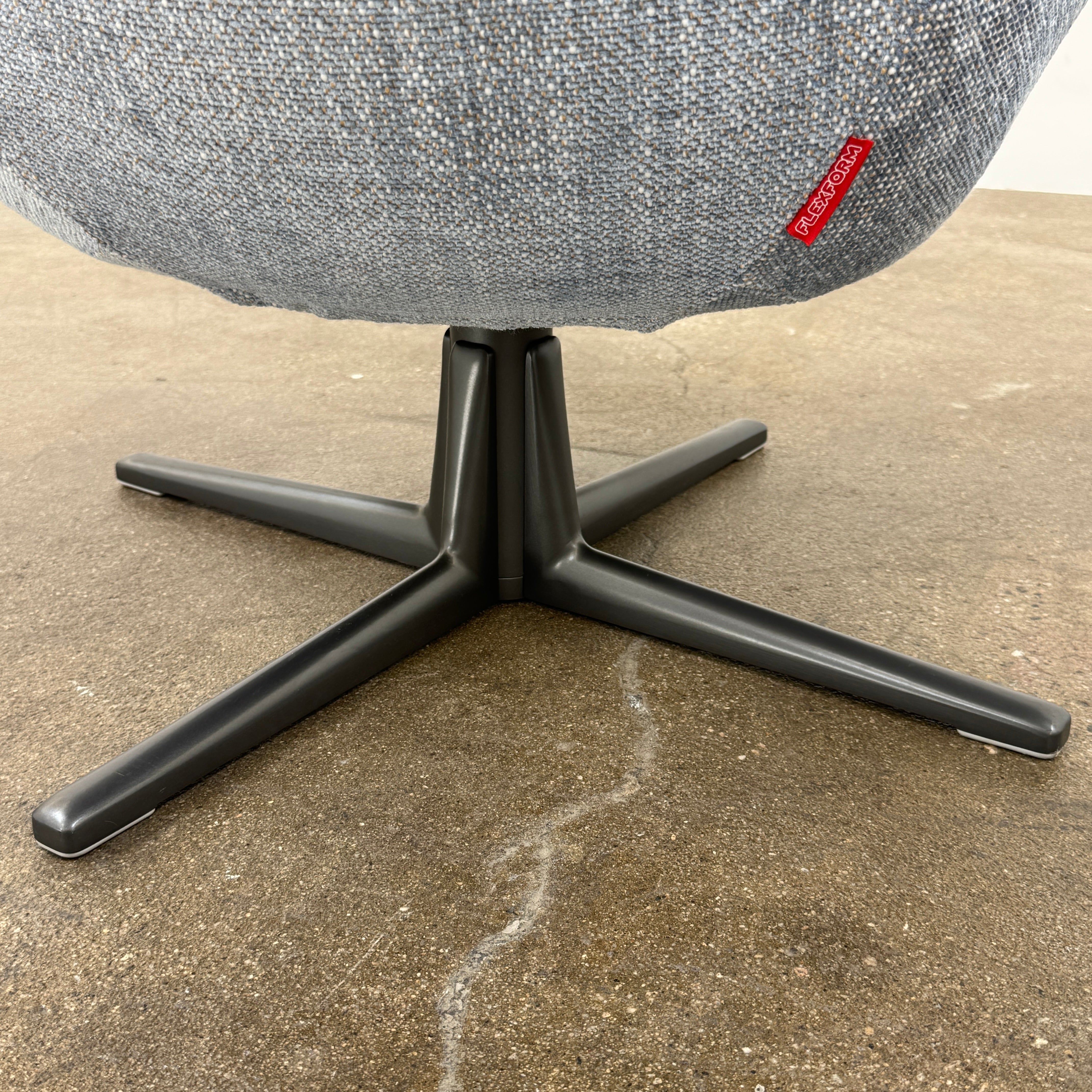 The Flexform Marlon Swivel Armchair and Ottoman, available with two covers, feature ergonomic design and black metal bases from Flexform, shown here in a modern gray finish against a plain white background.