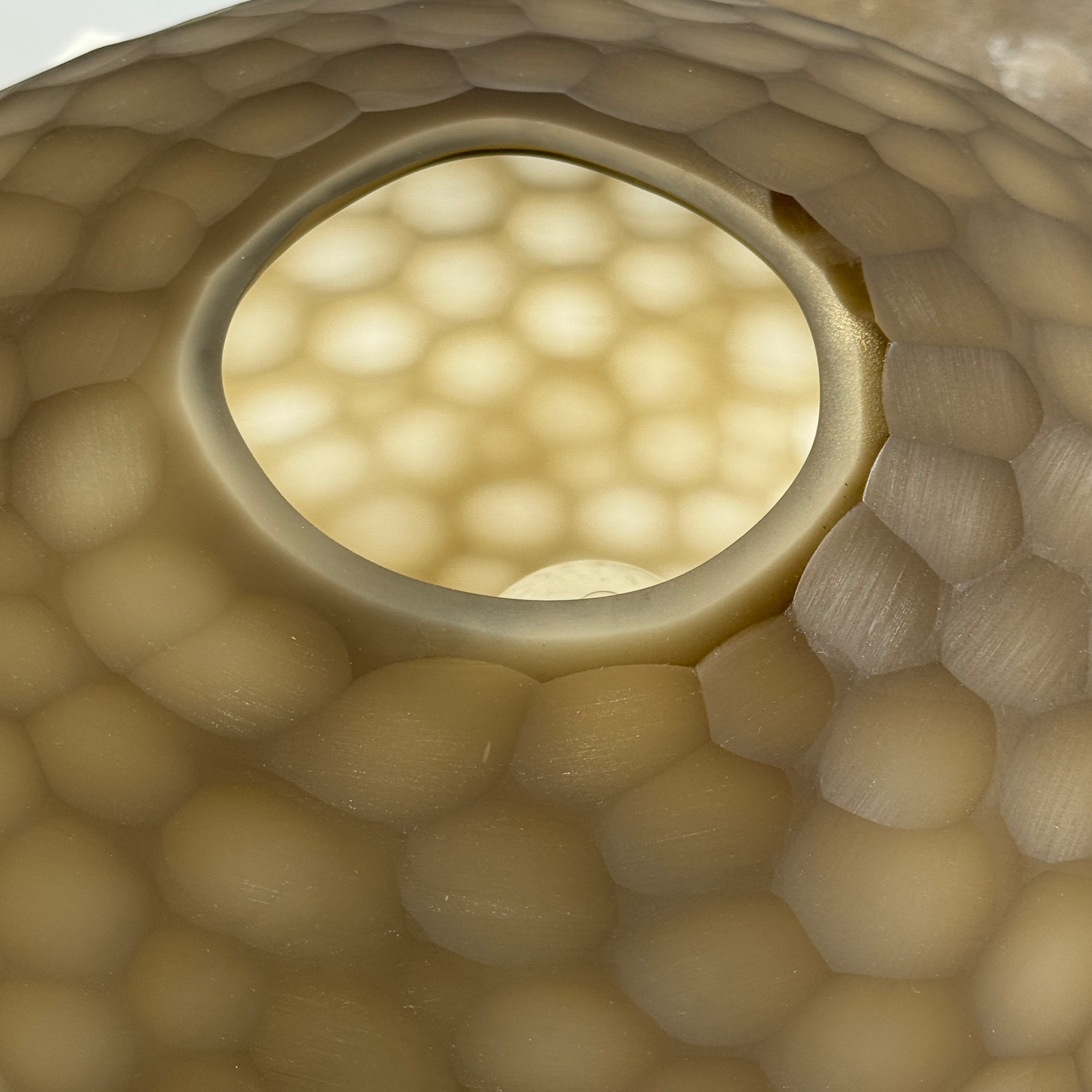 The Guax Erbse 2 Table Lamp by Guax features a mouth-blown, honeycomb-patterned glass shade on a round metal base, with an exposed black power cord for a touch of modern elegance.