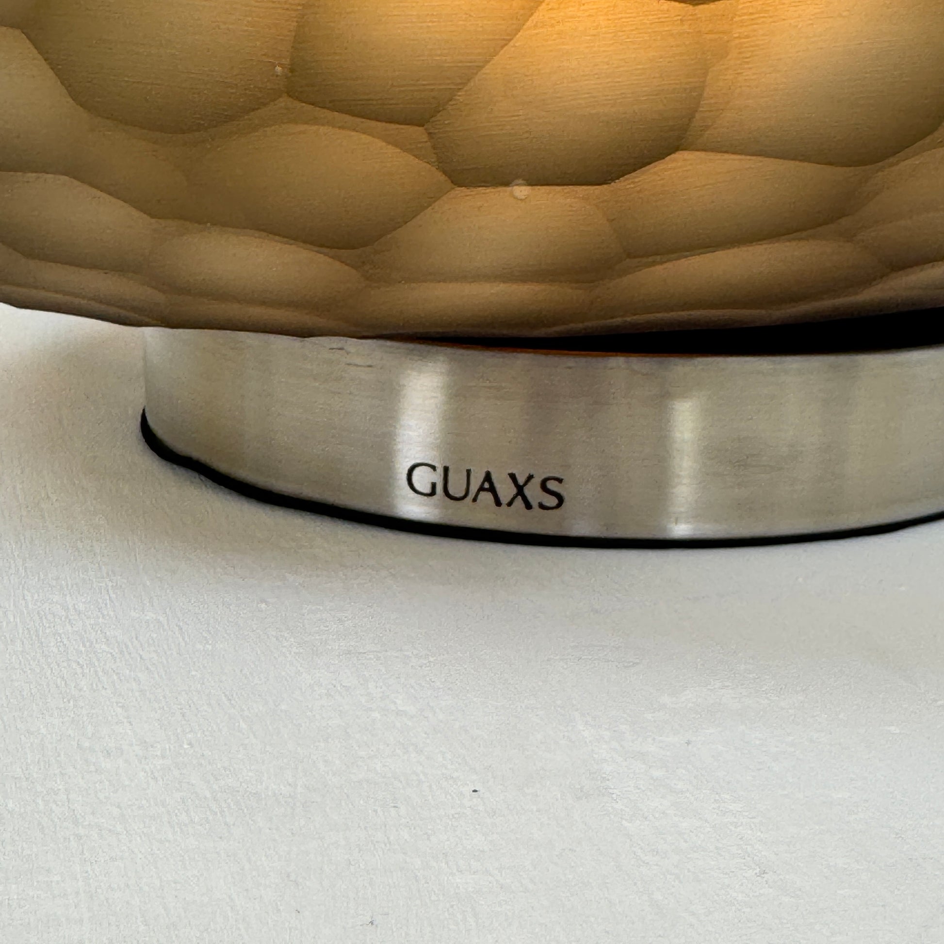 The Guax Erbse 2 Table Lamp by Guax features a mouth-blown, honeycomb-patterned glass shade on a round metal base, with an exposed black power cord for a touch of modern elegance.