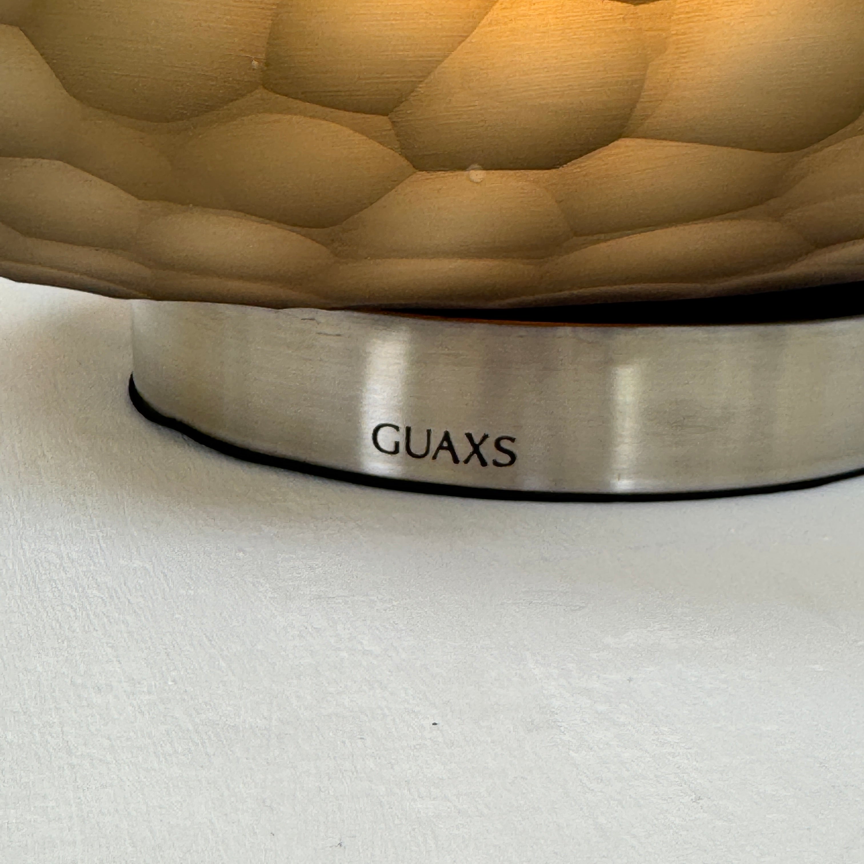 The Guax Erbse 2 Table Lamp by Guax features a mouth-blown, honeycomb-patterned glass shade on a round metal base, with an exposed black power cord for a touch of modern elegance.