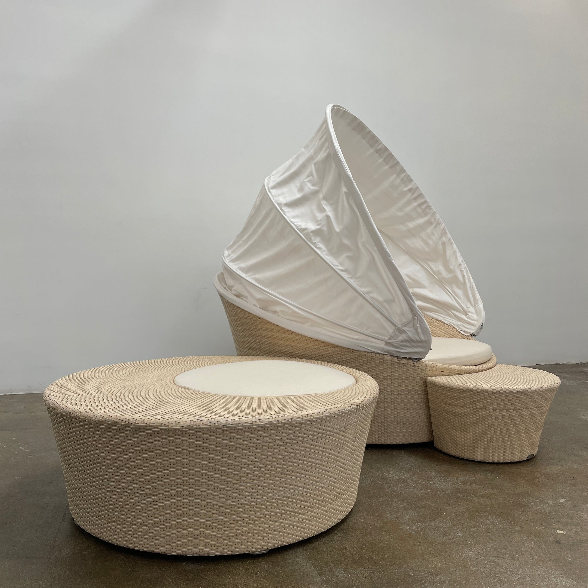 Experience the elegance of Richard Frinier Design with Dedon's Orbit Swivel Sofa Set, including a curved sofa with an adjustable canopy, ottoman, and side table. Cream-colored cushions add style and comfort to your outdoor ensemble.