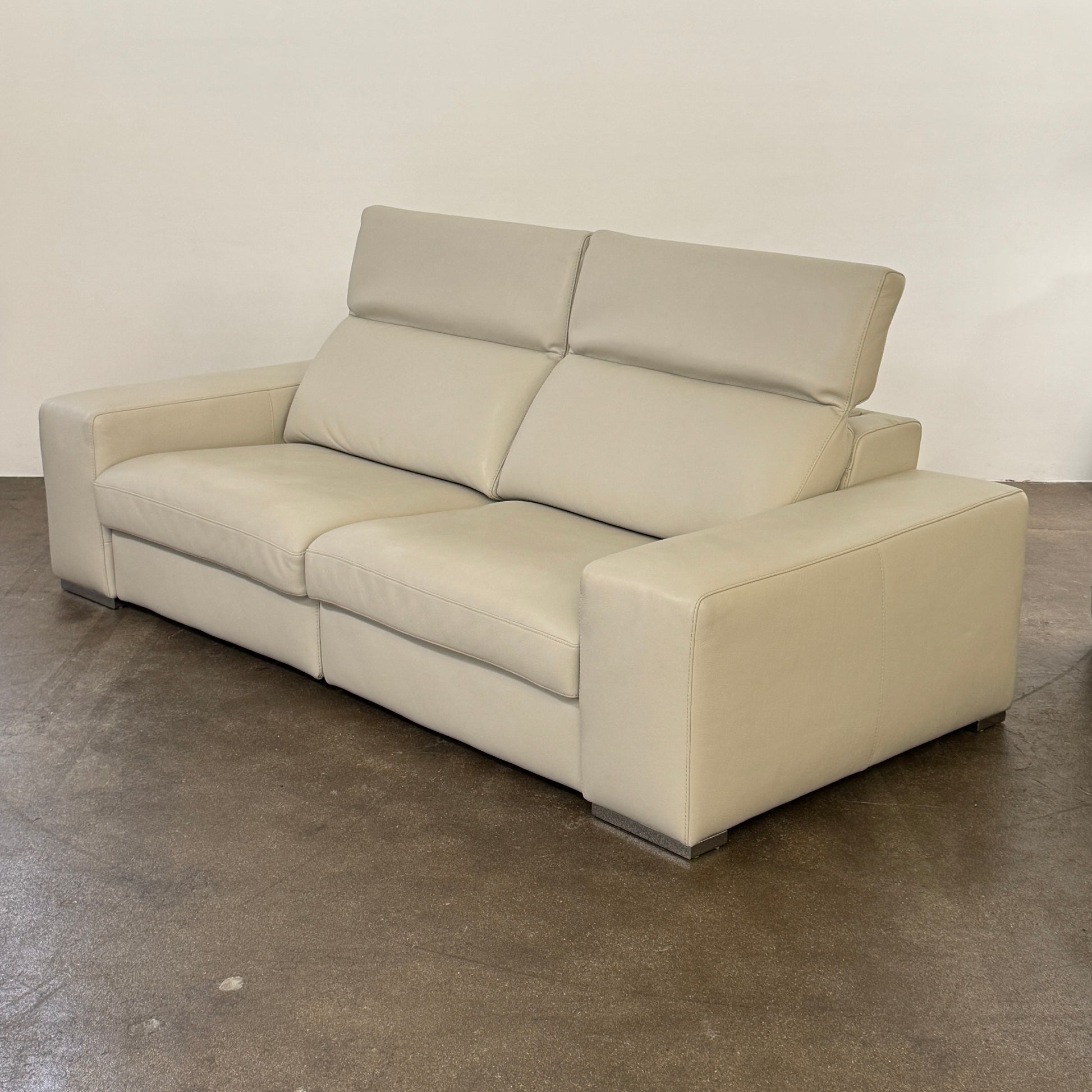 The Roche Bobois Leather Sofa With Movable Headrest features a modern beige design, wide armrests, metal legs, and an adjustable headrest—ideal for any contemporary living space.