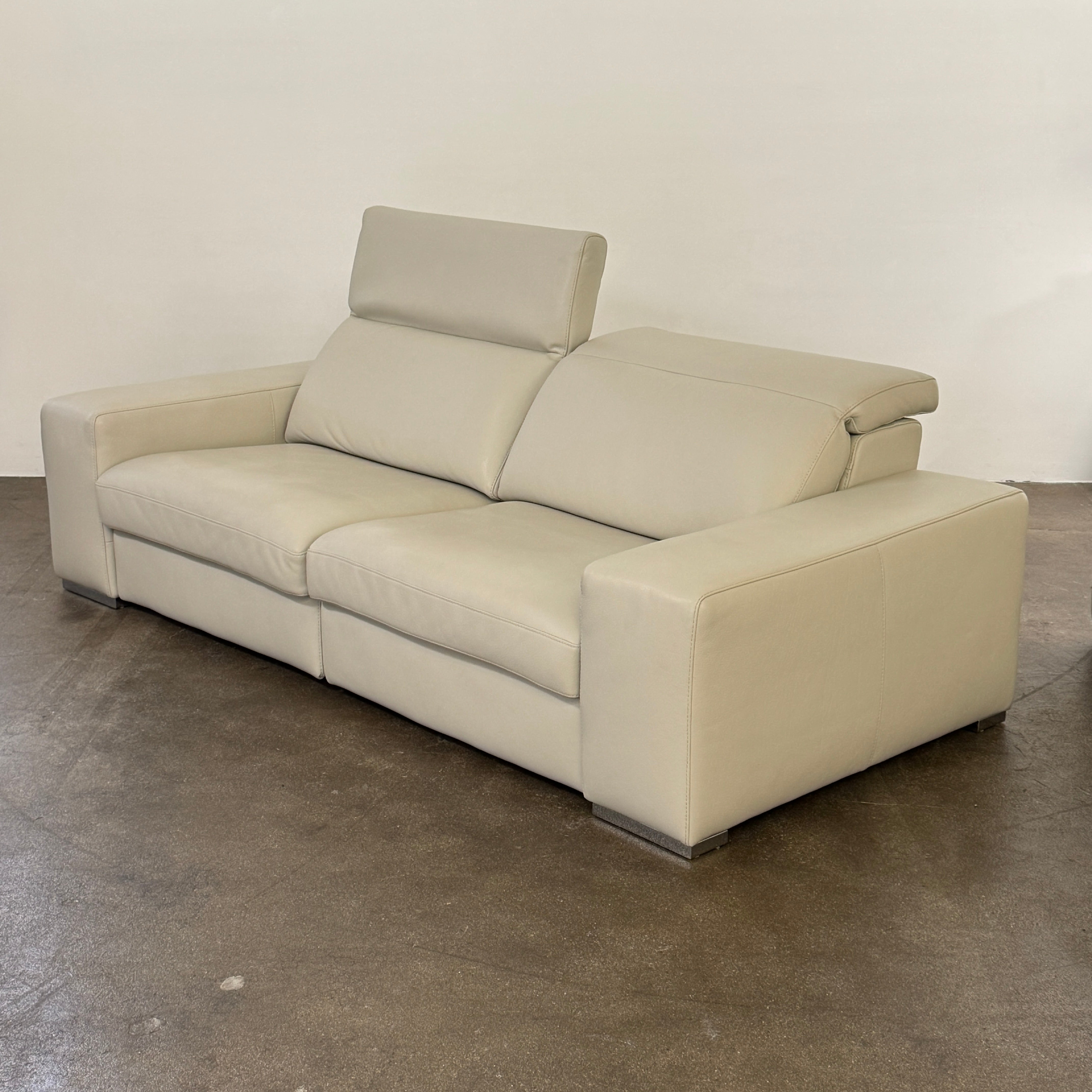 The Roche Bobois Leather Sofa With Movable Headrest features a modern beige design, wide armrests, metal legs, and an adjustable headrest—ideal for any contemporary living space.