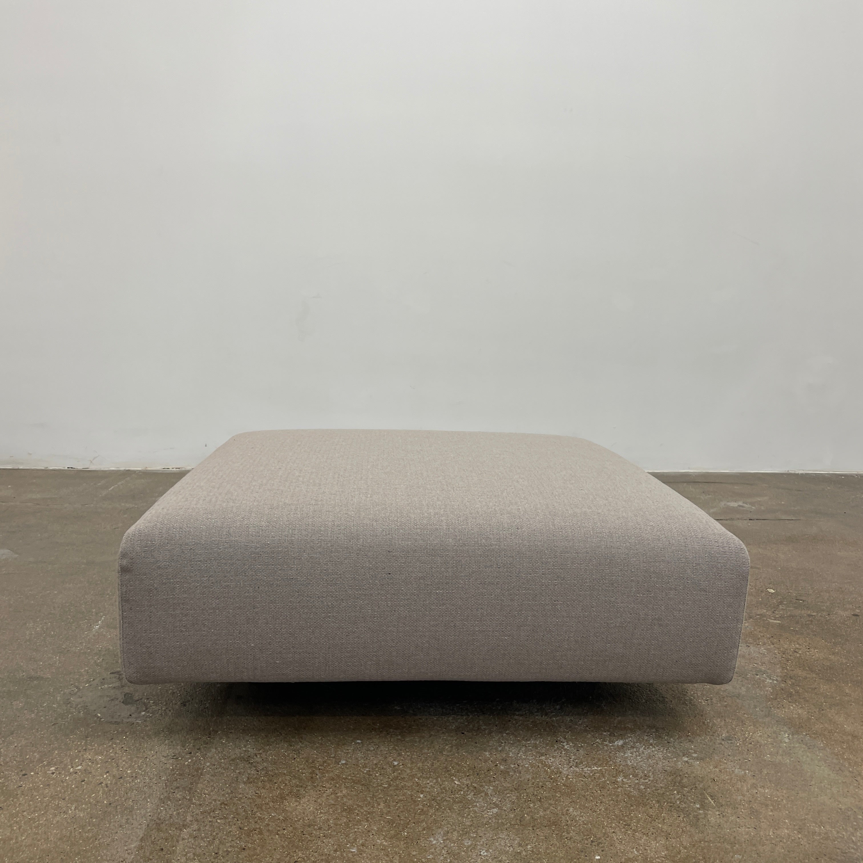 A minimalist gray Paola Lenti Orlando sofa bench from Modern Resale, featuring a 37" square design with one backrest and two rectangular cushions, is set against a plain white background.